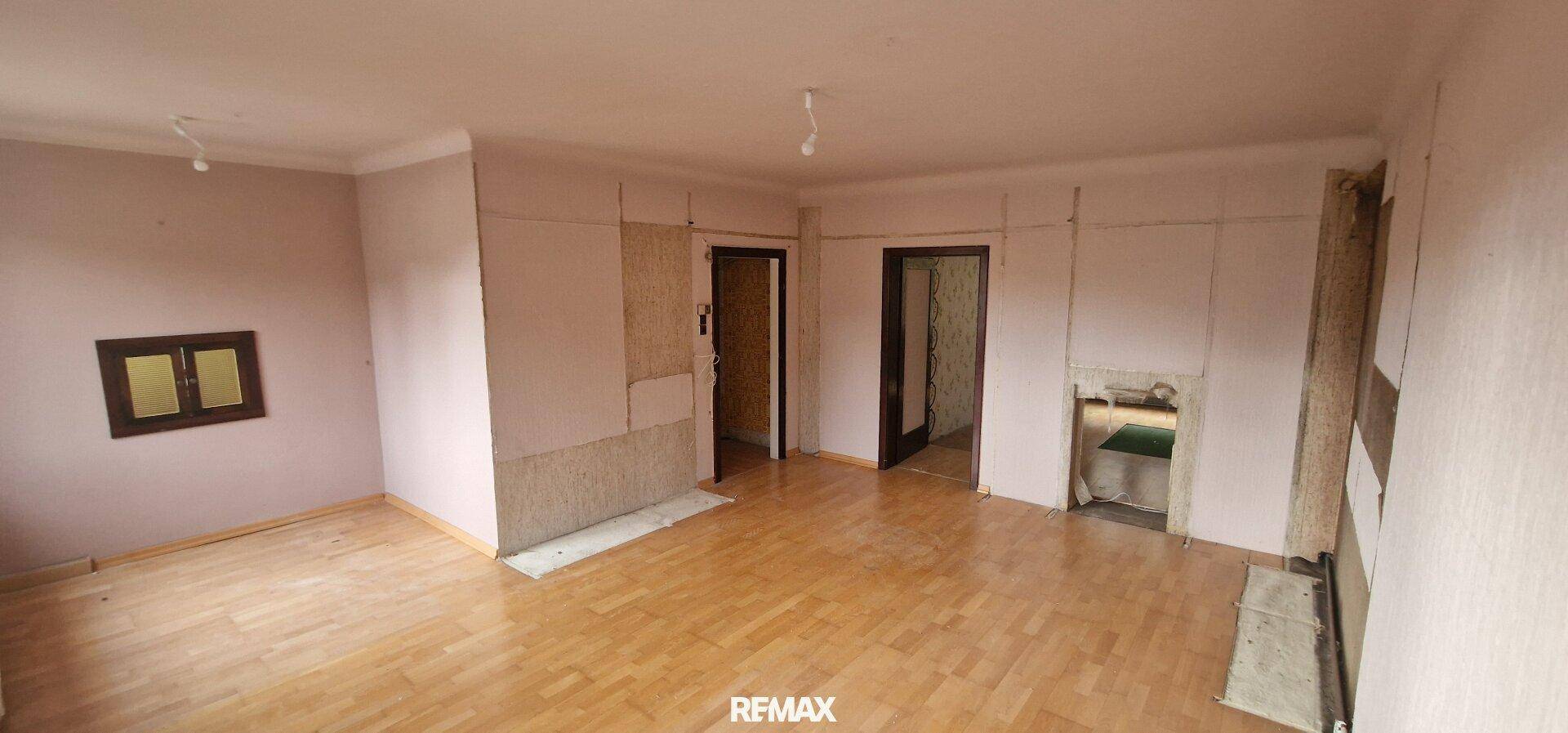 Geräumiger Raum mit Holzboden und teilweise entfernter Tapete, bereit für eine umfassende Renovierung.