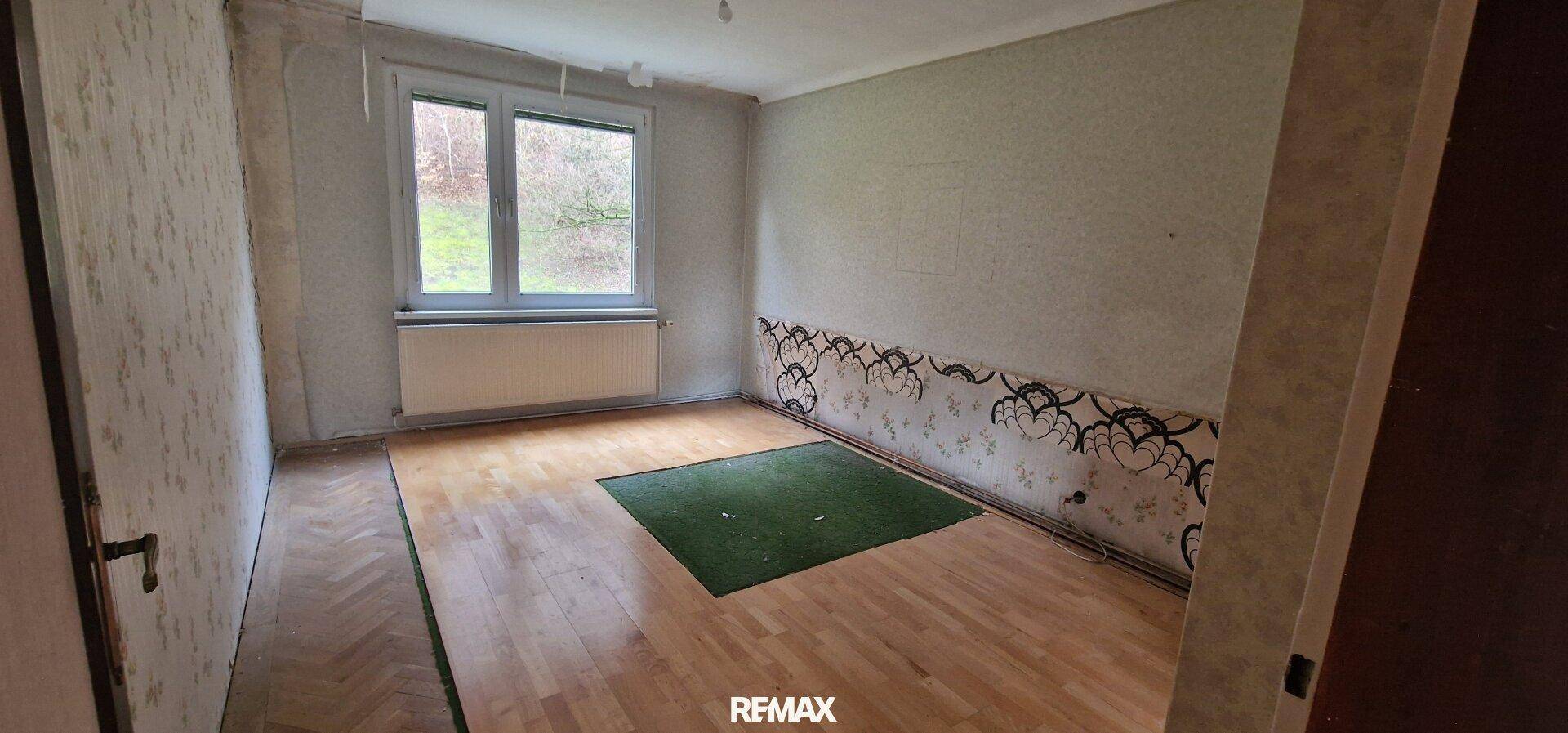 Schlafzimmer in Renovierung mit Holzboden, Fenster und Resten alter Tapete, hell und geräumig.