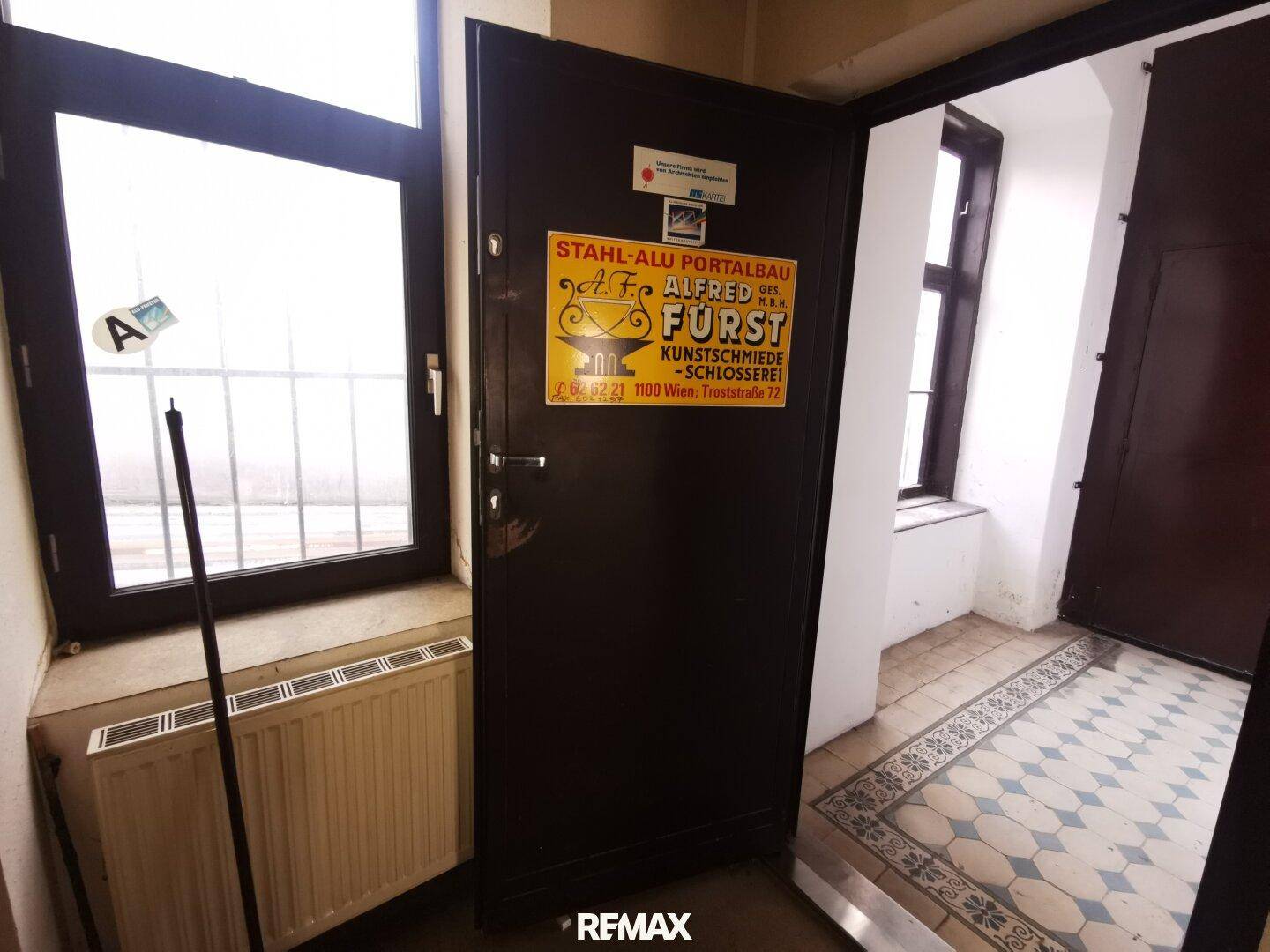 Eingangsbereich mit gemustertem Fliesenboden, dunkler Tür und Fenster.