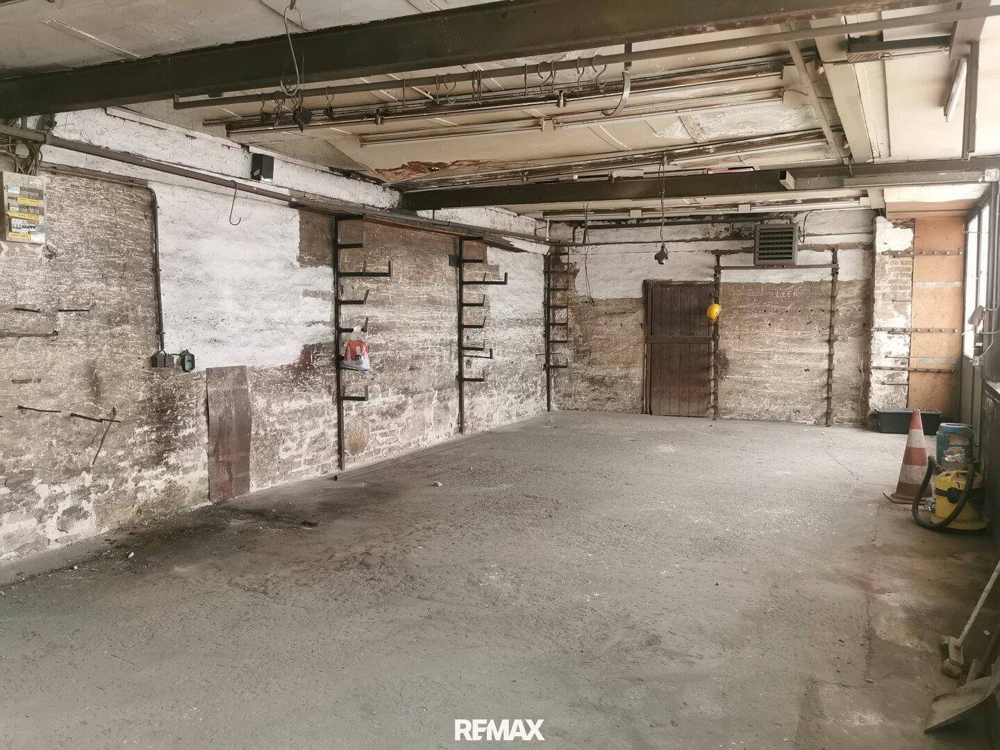 Weiterer Blick in den großen Lagerraum mit Betonboden, rauen Wänden und Metallregalen, die an der Wand befestigt sind.