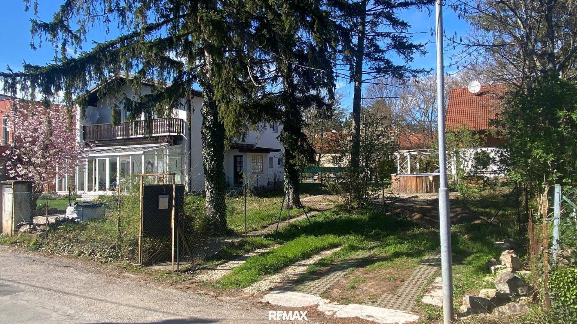 Ansicht des Wohnhauses von der Straße mit Einfahrt, Garten, Balkon und einem Wintergarten an der Seite.