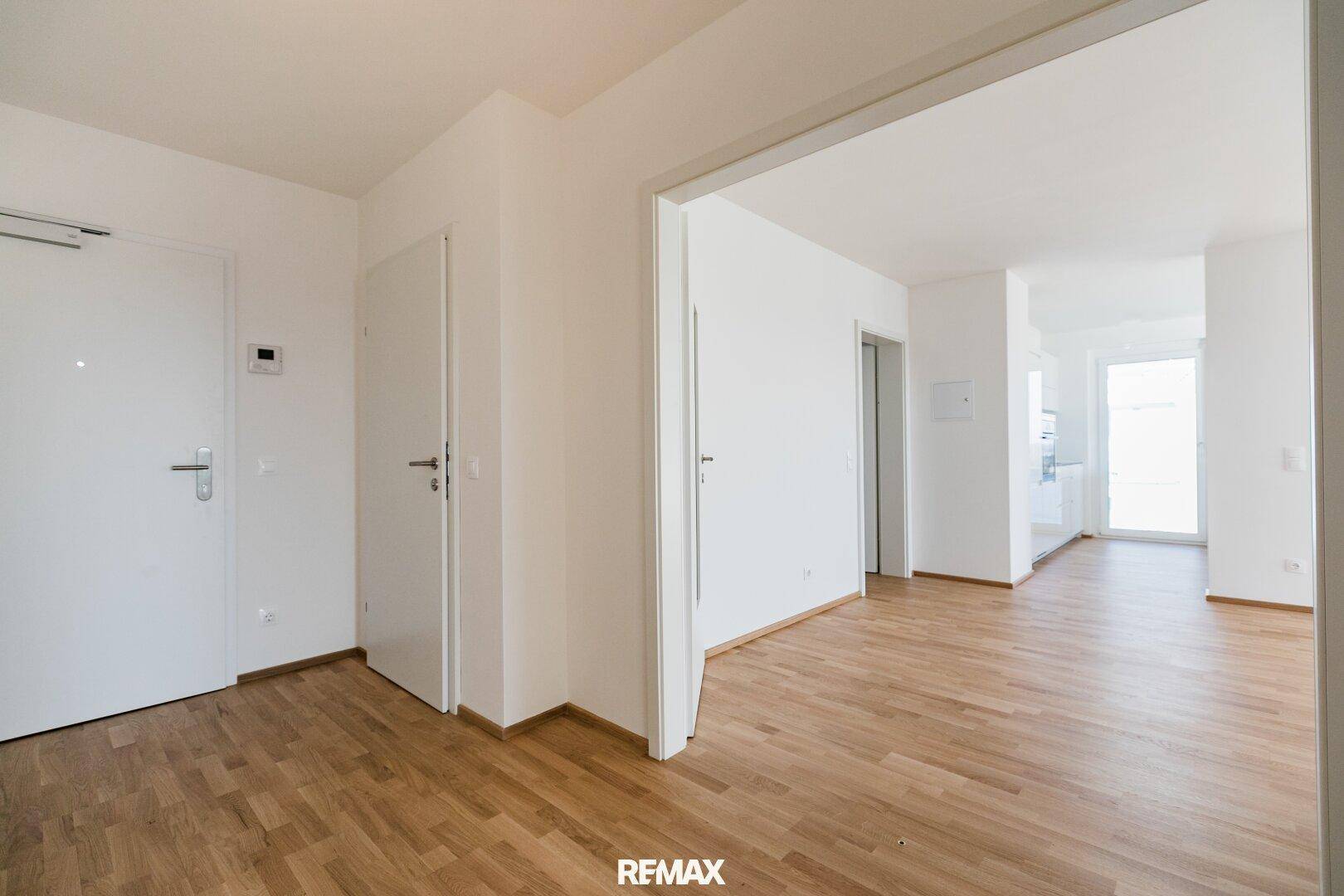 Heller Eingangsbereich mit Holzboden und weißen Wänden, der zu den verschiedenen Räumen der Wohnung führt.