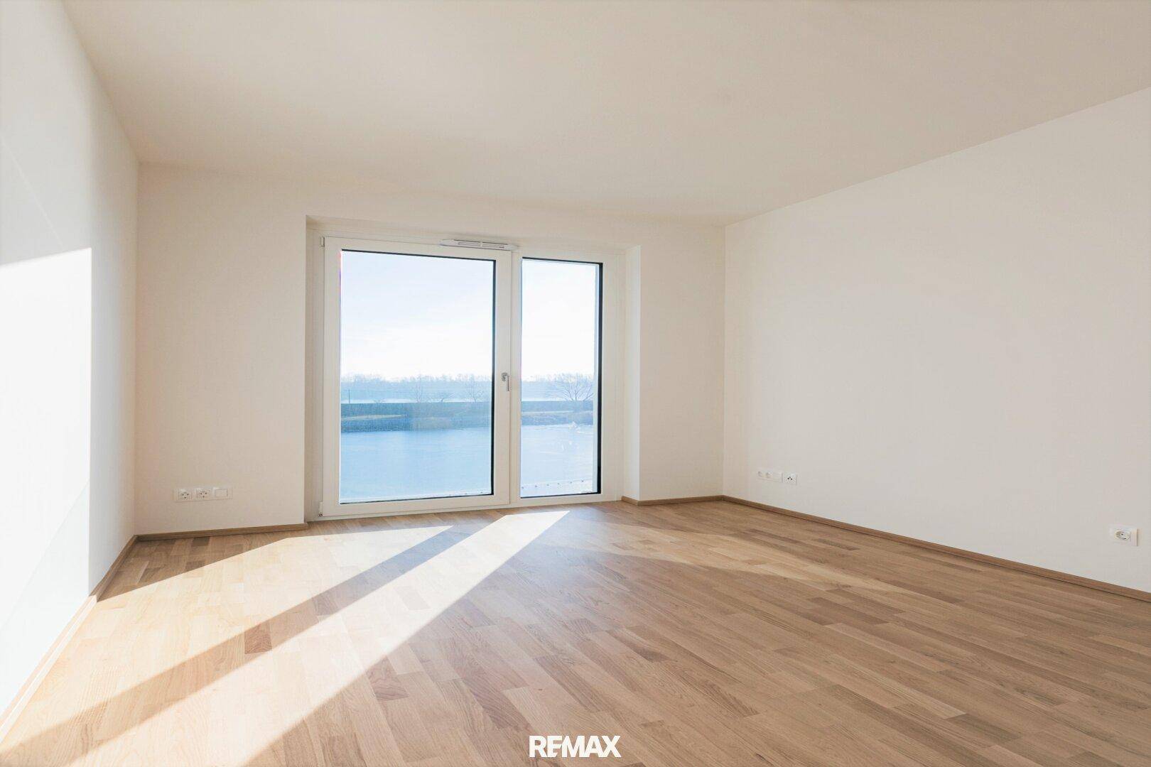 Helles, leeres Schlafzimmer mit Holzboden und großen Fenstern, die viel Tageslicht und einen weiten Blick bieten.