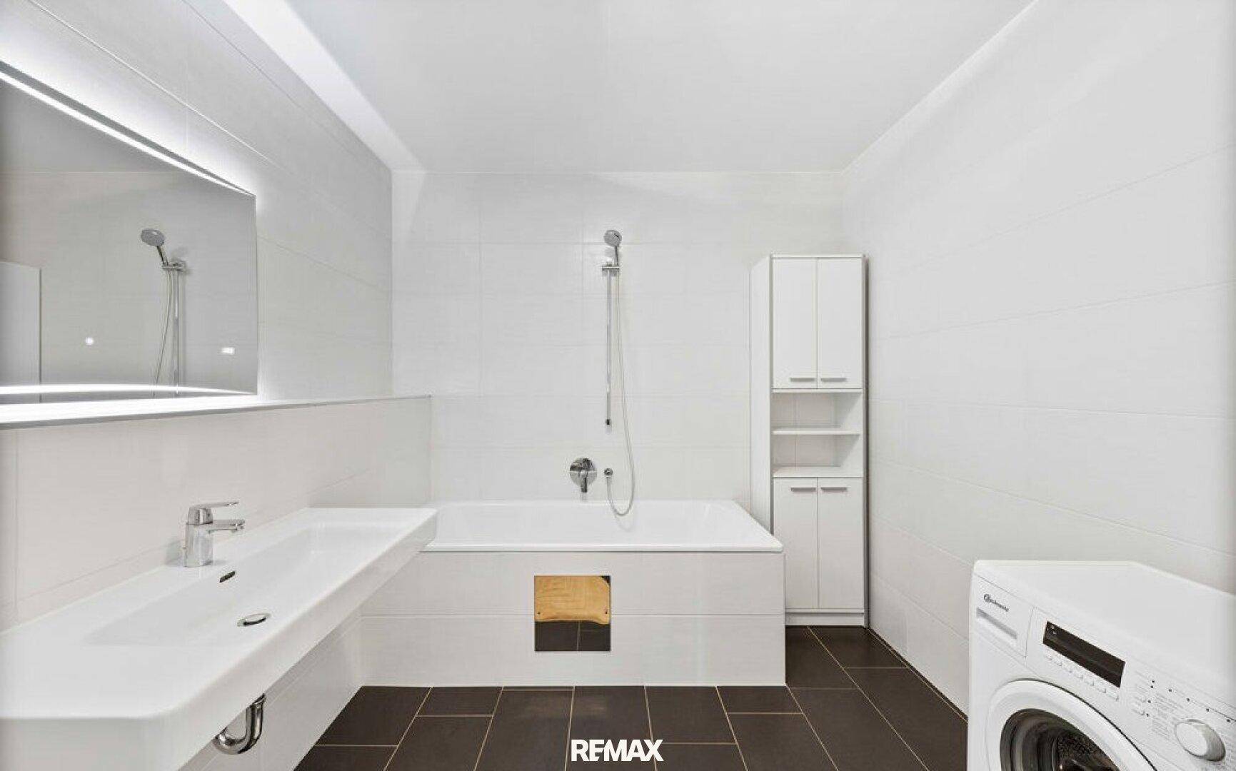 Helles Badezimmer mit Badewanne, Waschbecken und Waschmaschine, ausgestattet mit modernen Fliesen.