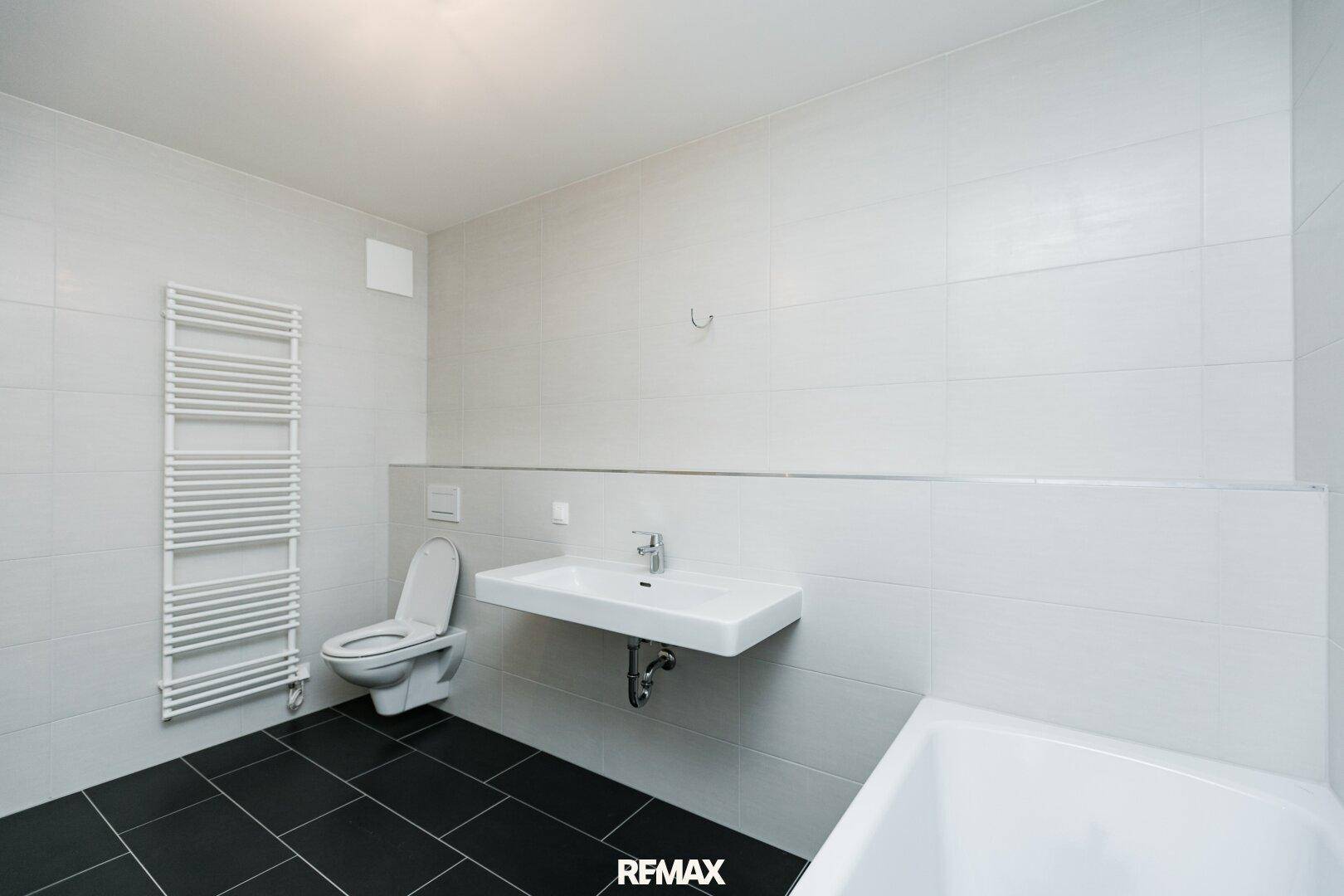 Modernes Badezimmer mit Wand-WC, Waschbecken und beheiztem Handtuchhalter, hell gefliest.