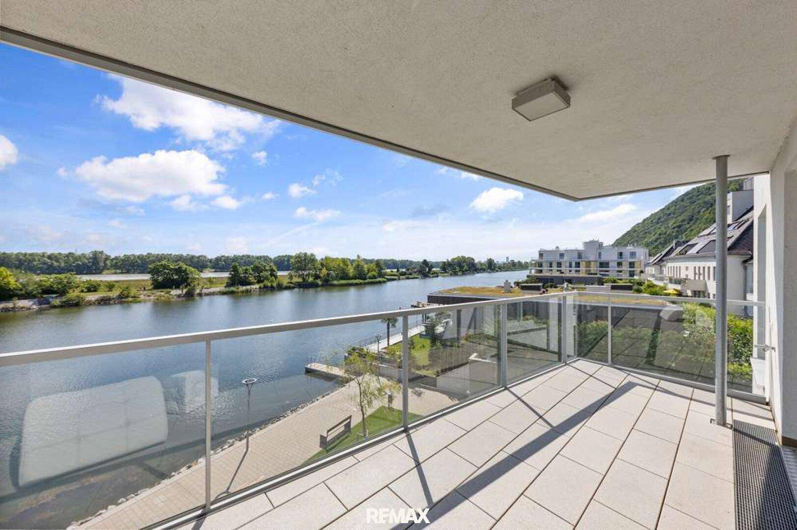 Großer Balkon mit Fliesenboden und Glasgeländer, bietet einen weiten Blick auf den Fluss und die umliegende Landschaft.