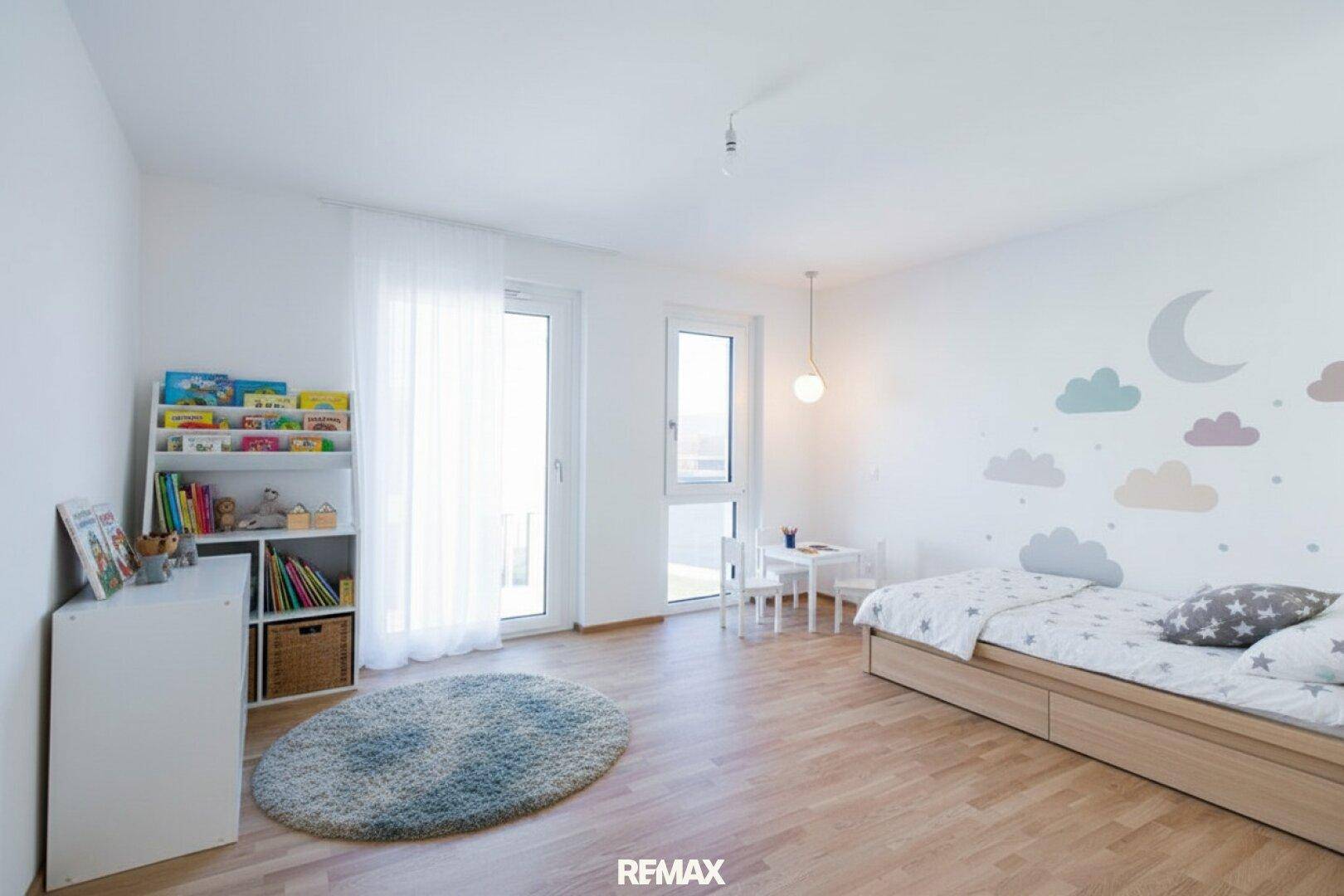 Freundliches Kinderzimmer mit Holzboden, hellen Wänden und Zugang zu einem kleinen Balkon.