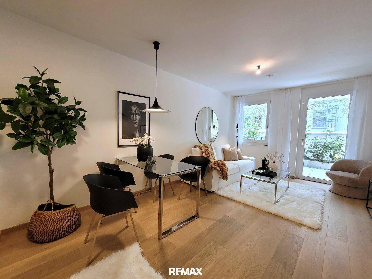 Offener Wohn-Essbereich mit Holzboden, bequemer Couch und viel Tageslicht durch große Fenster.