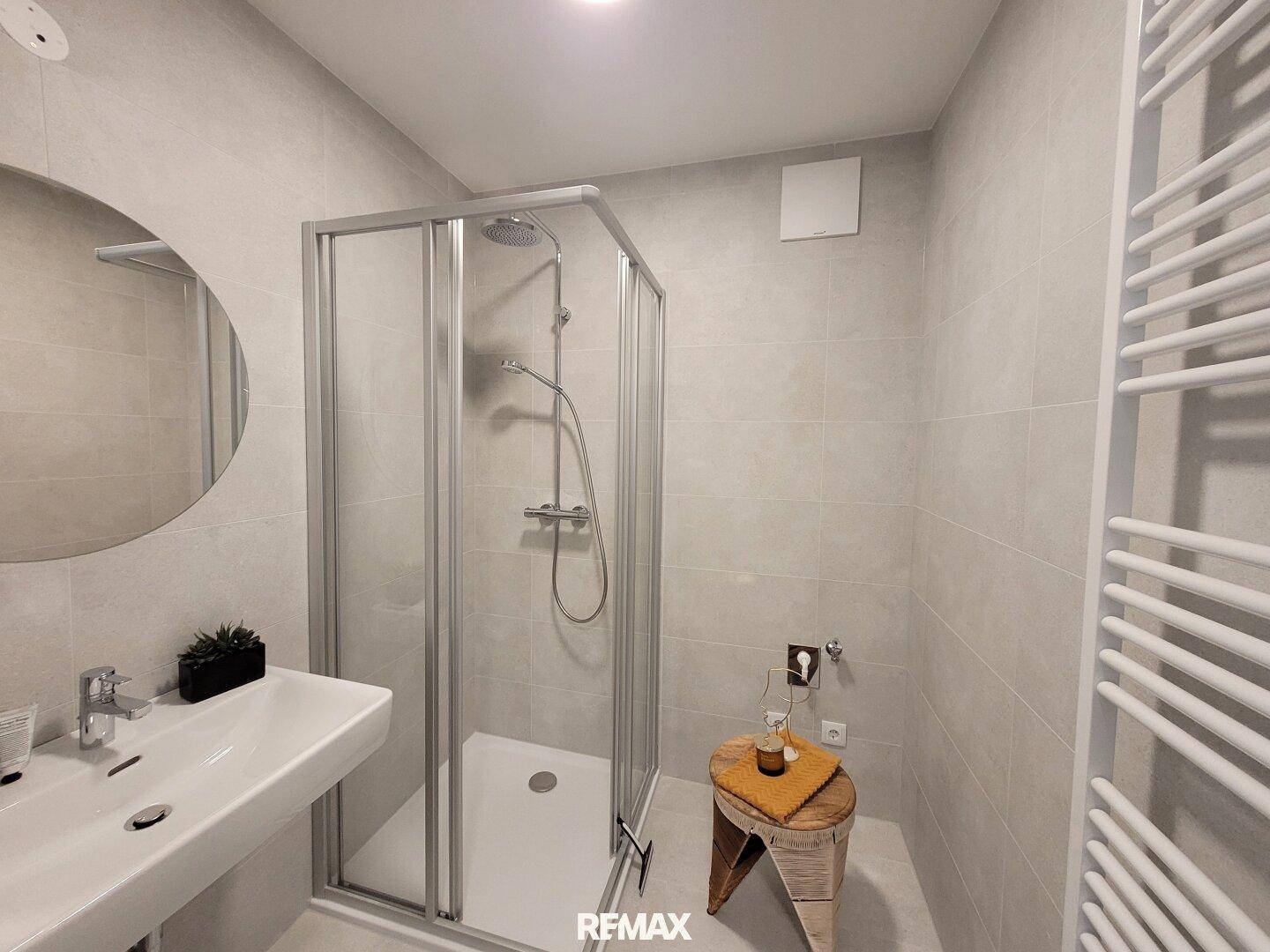 Modernes Badezimmer mit Duschkabine, Einzelwaschbecken und beheiztem Handtuchhalter.