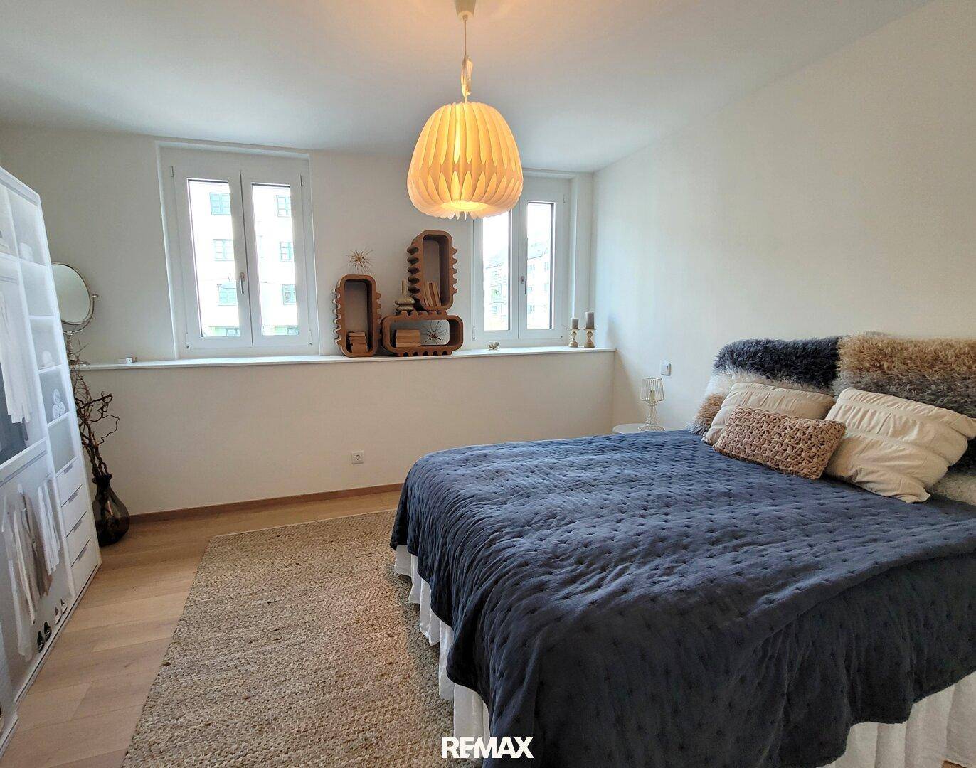 Schlafzimmer mit Holzboden, großen Fenstern und einem gemütlichen Bett mit weichen Textilien.