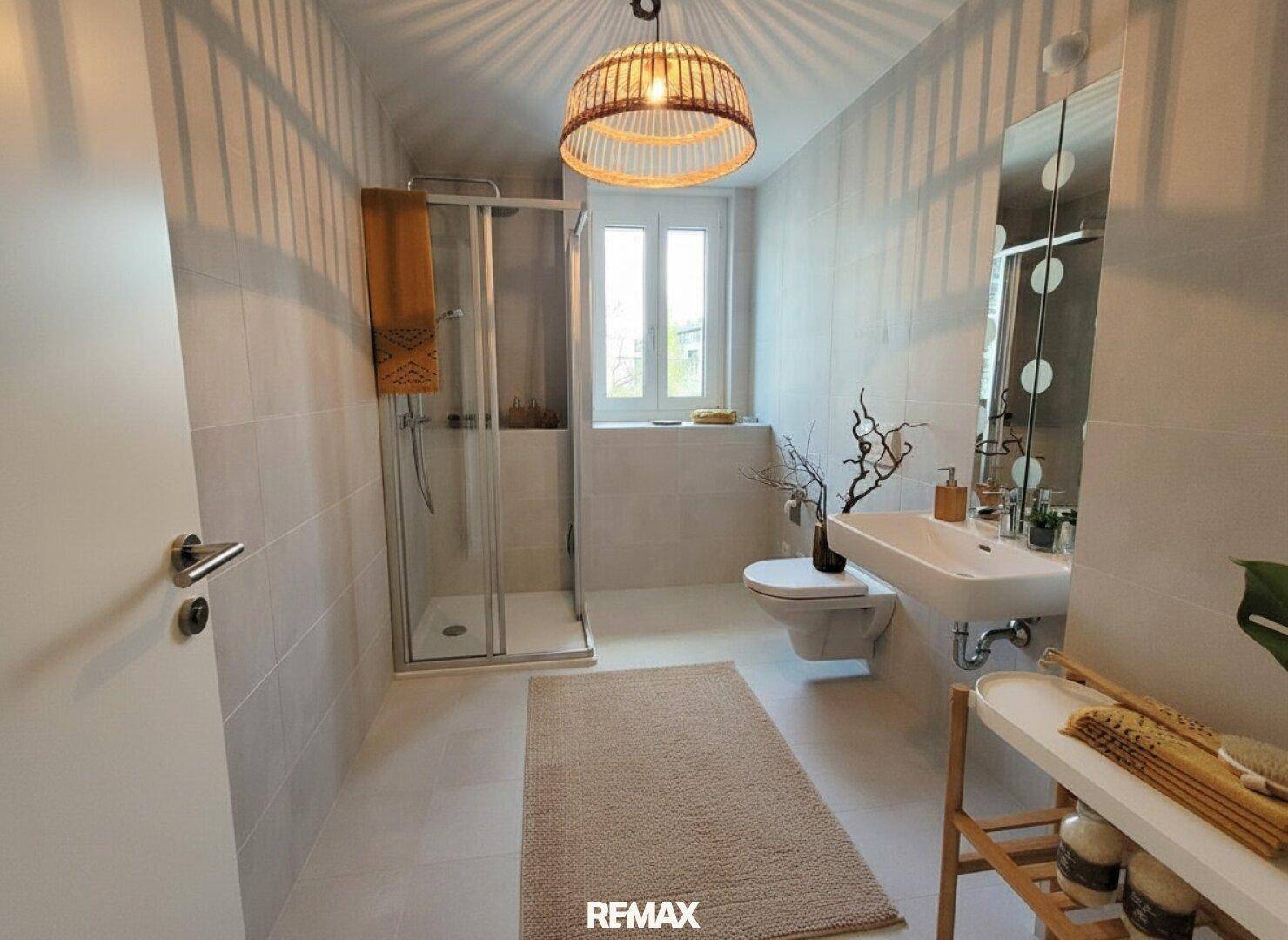 Modernes Badezimmer mit Duschkabine, Wand-WC, Waschbecken und Fenster für Tageslicht.