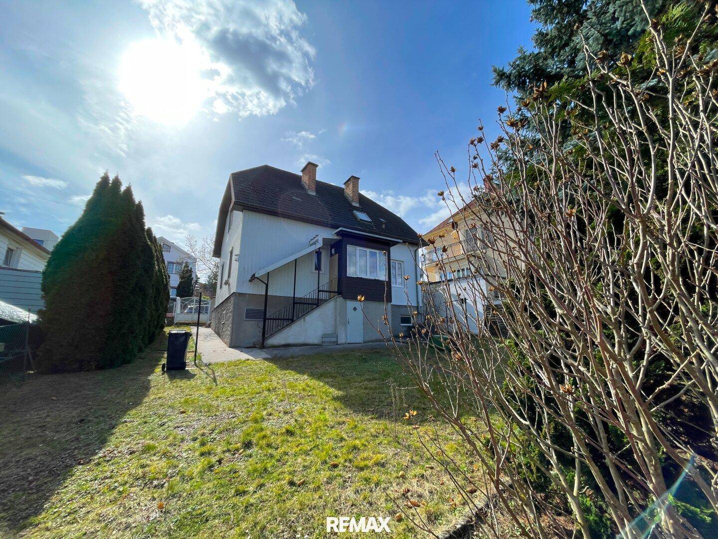 Sonniger Gartenbereich neben dem Haus mit Rasenfläche und Bäumen.