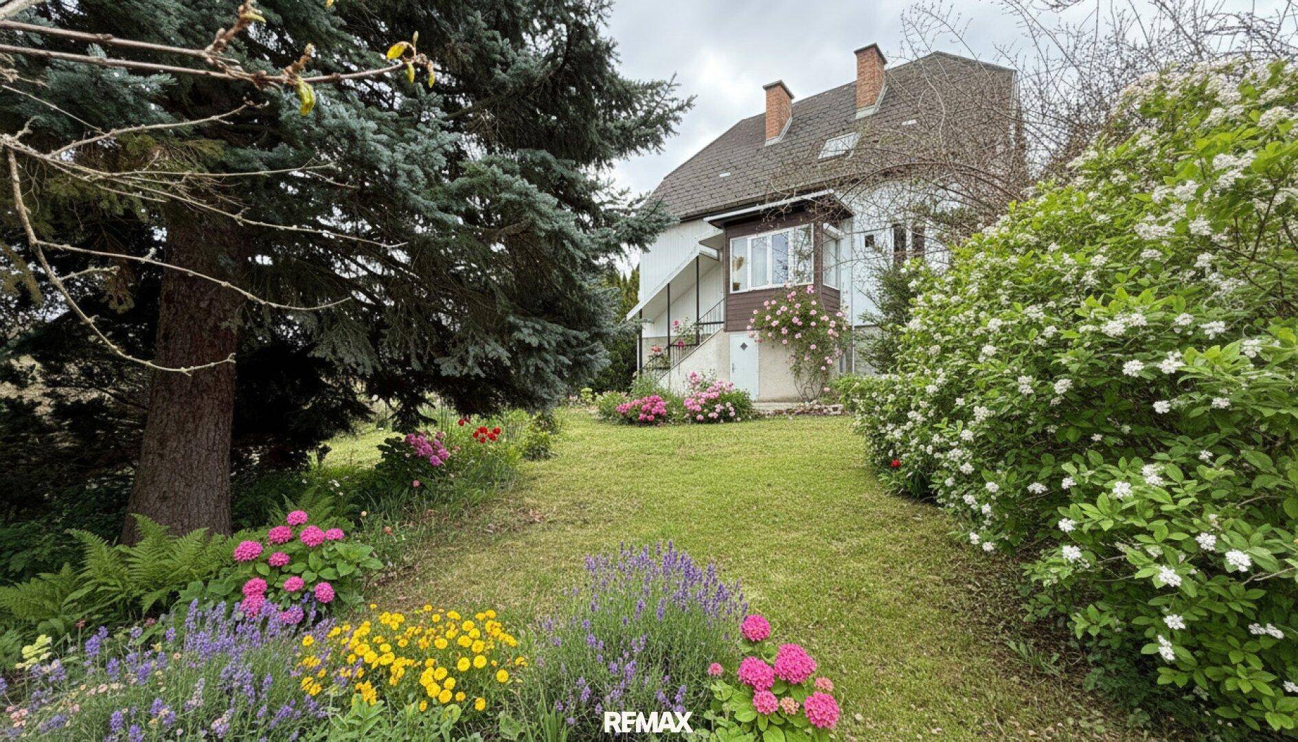 Blühender Garten mit verschiedenen Blumen und Blick auf das Einfamilienhaus.