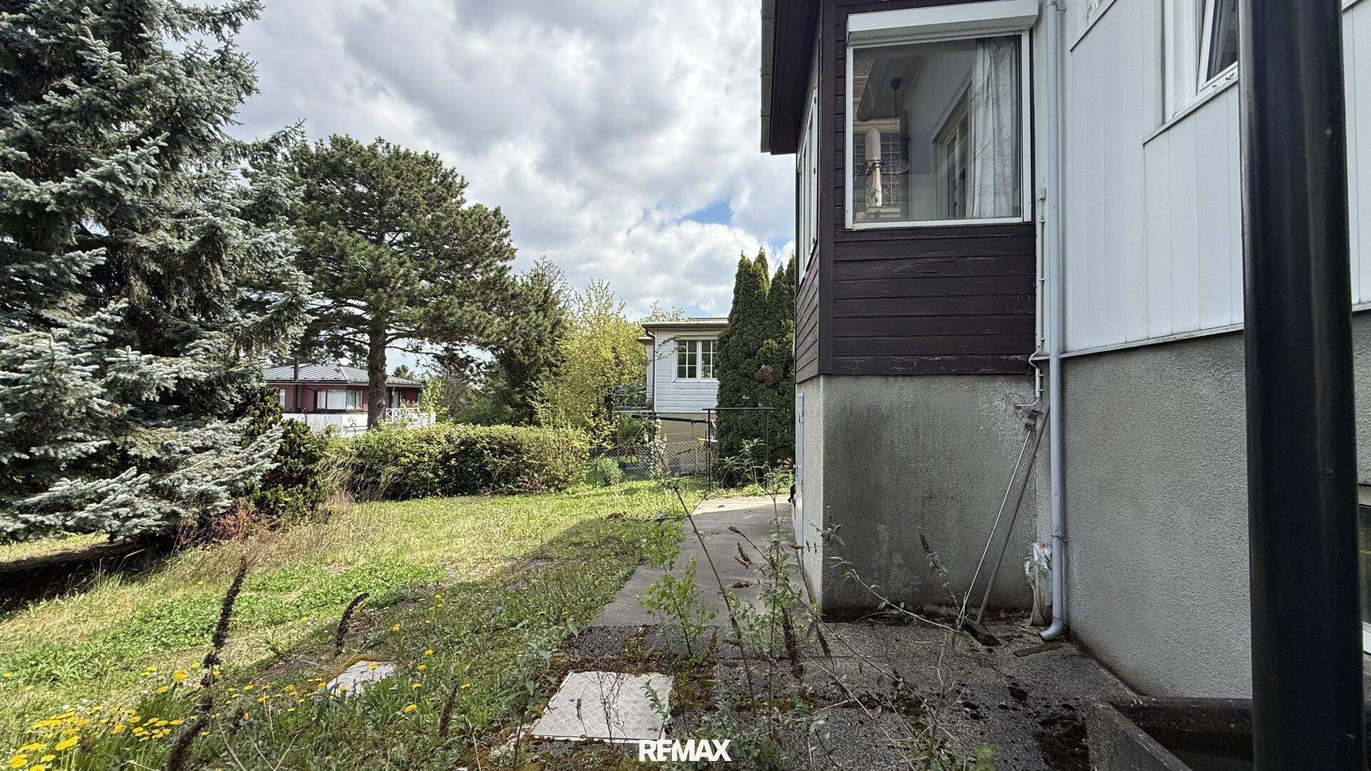 Pfad neben dem Haus, der zum verwilderten Gartenbereich führt.