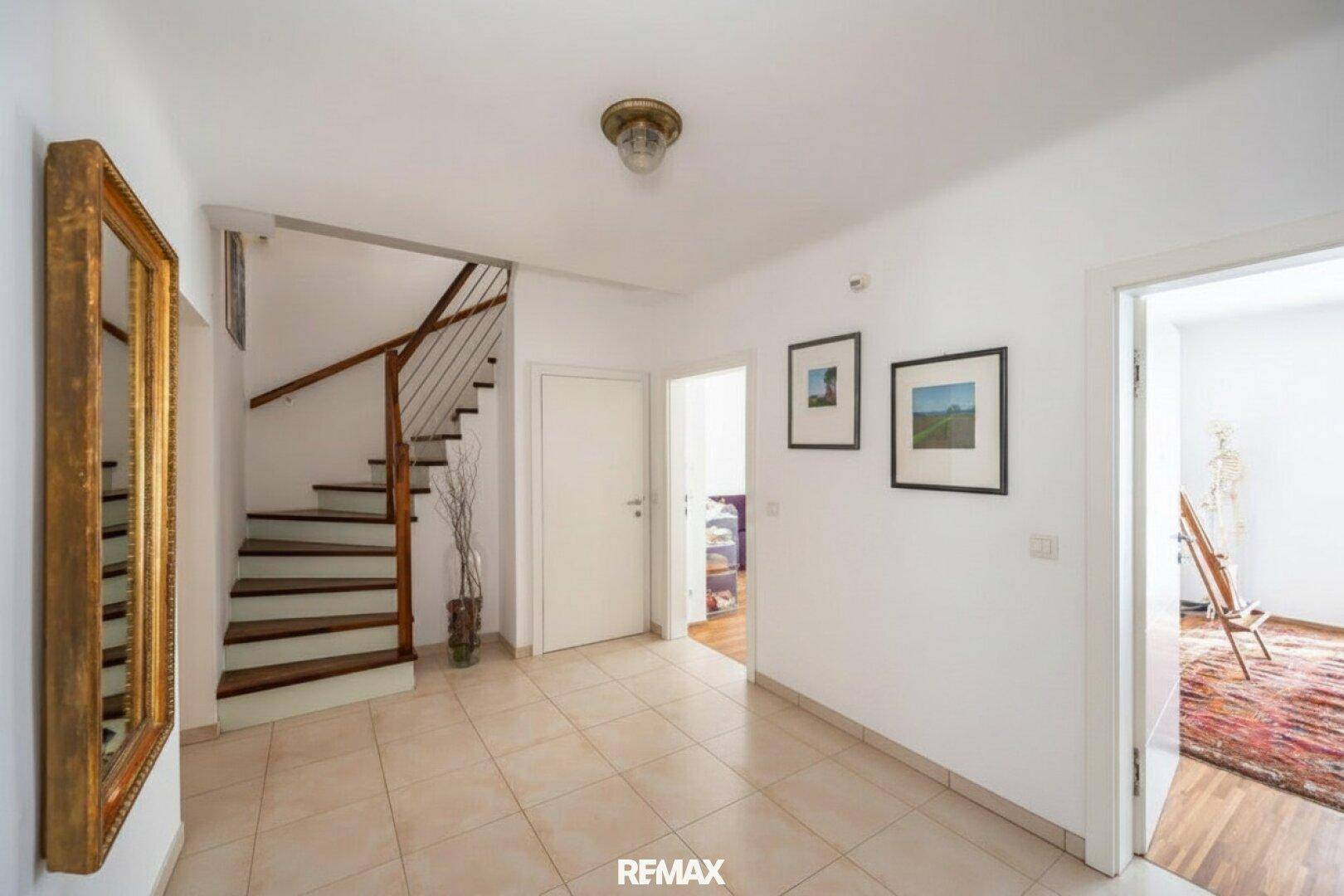 Heller Flur mit Fliesenboden und einer eleganten Holztreppe, die in die obere Etage führt.