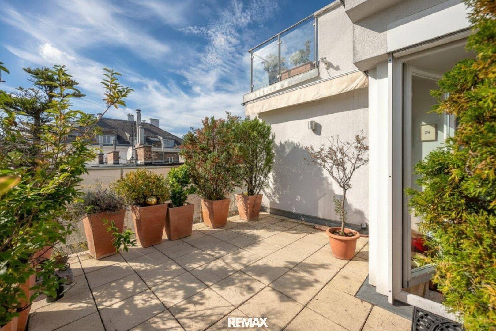 Geräumige Terrasse mit hellen Fliesen, vielen Pflanzen und Glasgeländer für entspannte Stunden.