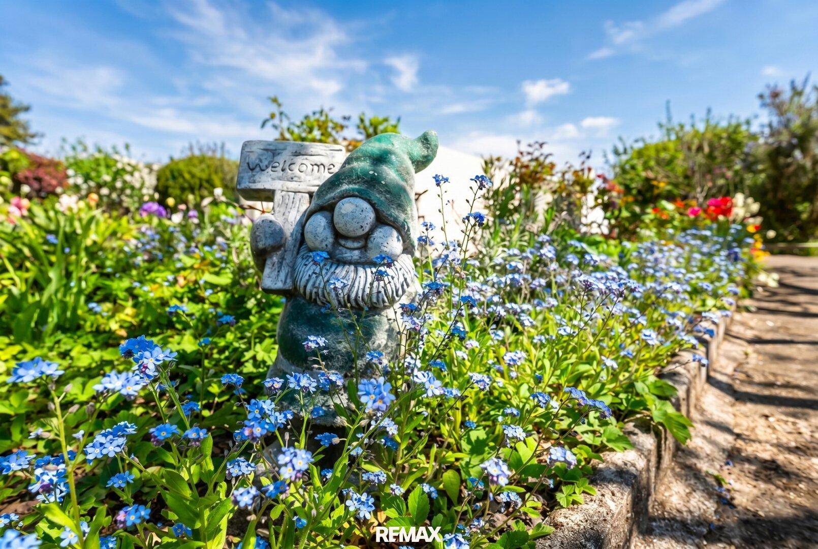 Detailaufnahme eines Gartenzwergs inmitten blauer Vergissmeinnicht, die den Garten schmücken.