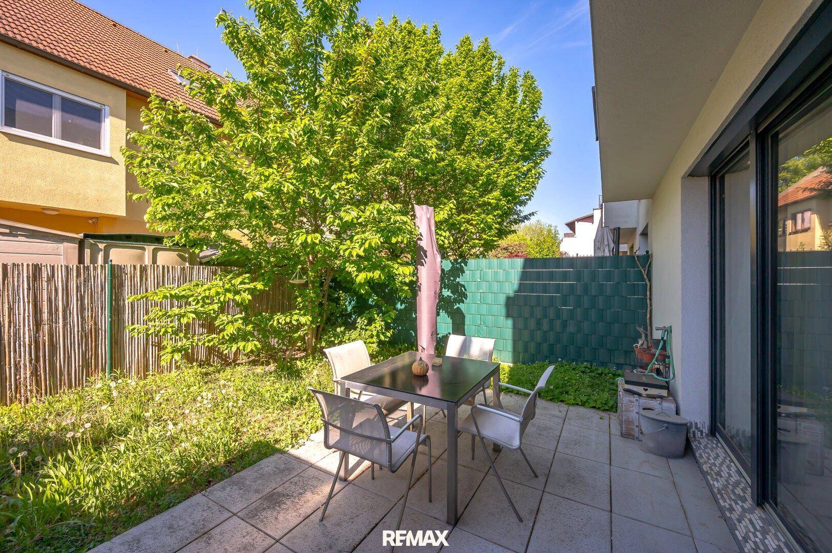 Gemütliche Terrasse mit Gartenmöbeln und Blick auf den grünen, eingezäunten Gartenbereich.