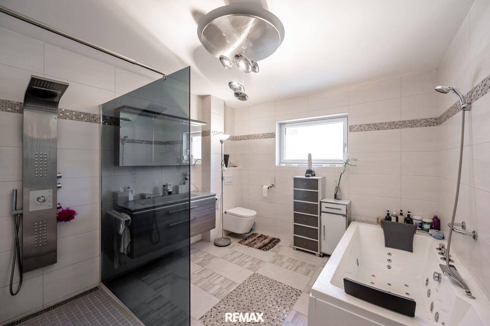 Modernes Badezimmer mit großer Dusche, Whirlpool-Badewanne und Fenster für Tageslicht.
