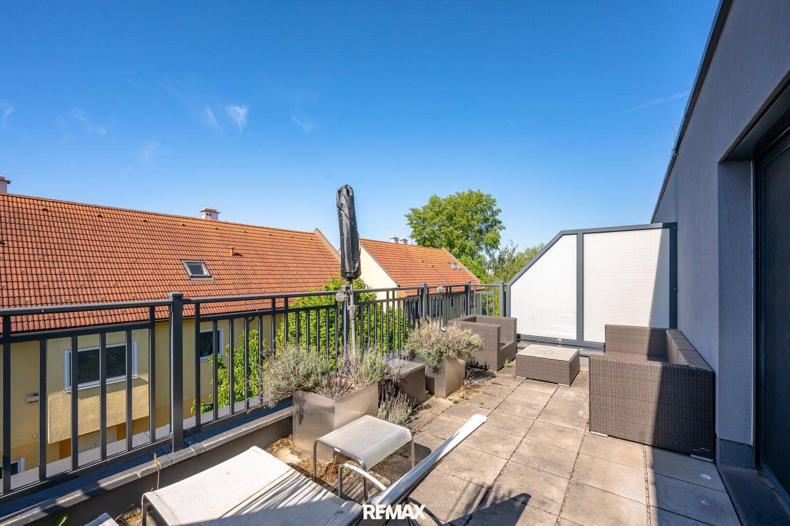 Sonnige Dachterrasse mit Loungemöbeln, Pflanzen und weitem Blick über die Dächer.