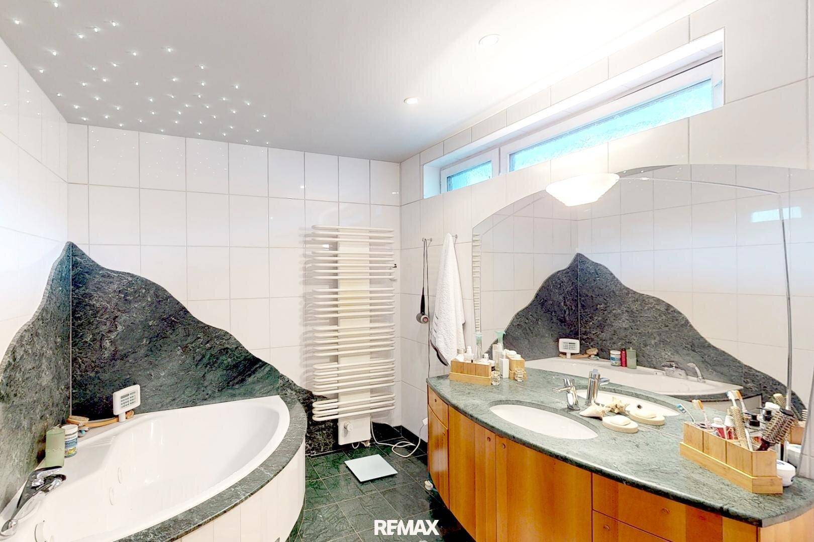Modernes Badezimmer mit Eckbadewanne, Doppelwaschbecken und grünen Marmoroberflächen unter Sternenhimmel-Beleuchtung.