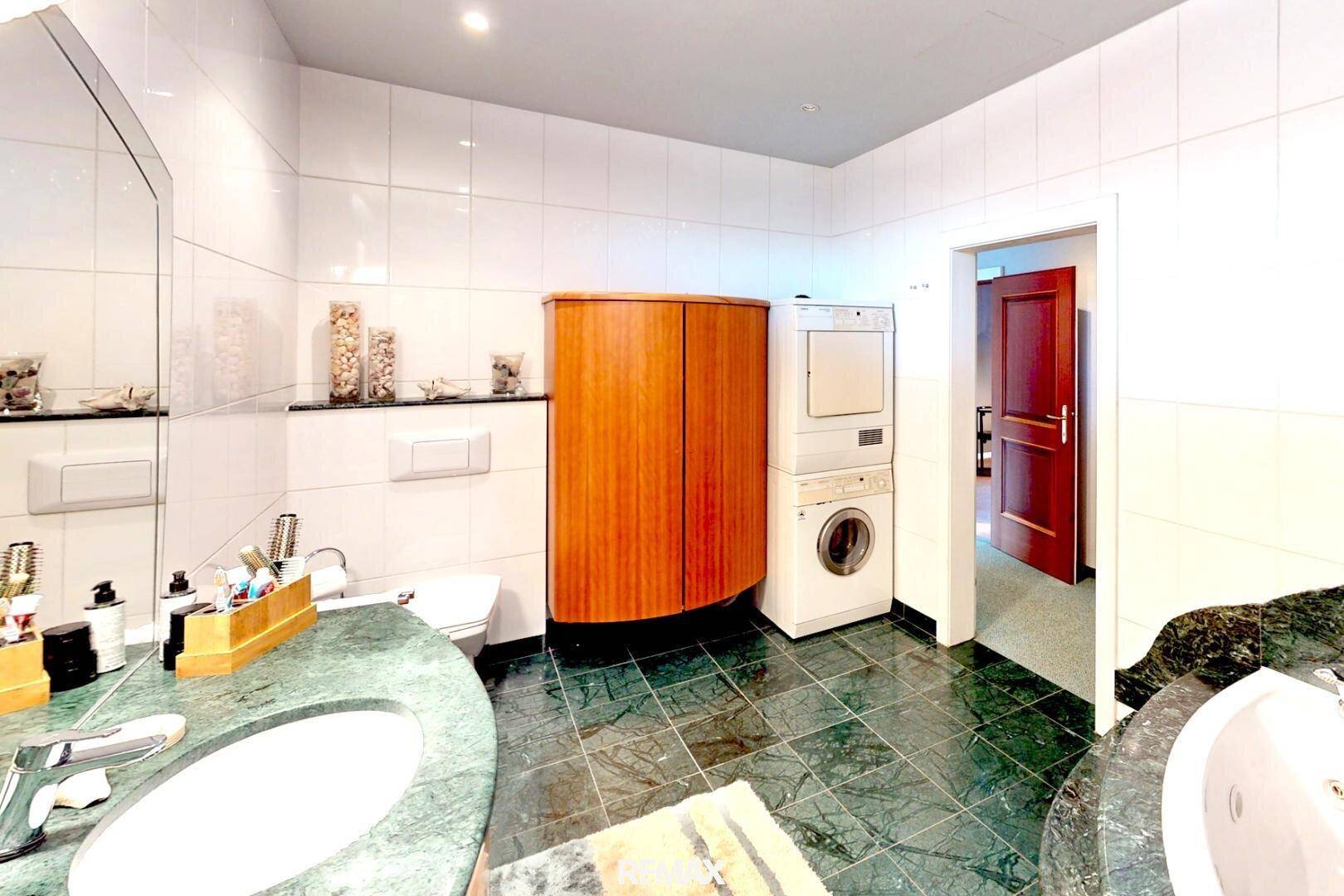 Funktionales Badezimmer mit Toilette, Waschmaschine, Trockner und grünen Fliesen am Boden.