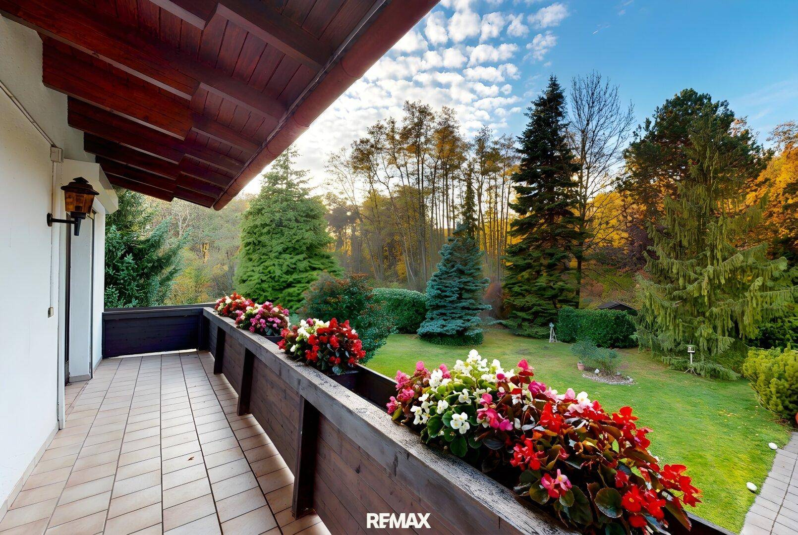Geräumiger Balkon mit Fliesenboden, Holzgeländer und bunten Blumenkästen mit Gartenblick.