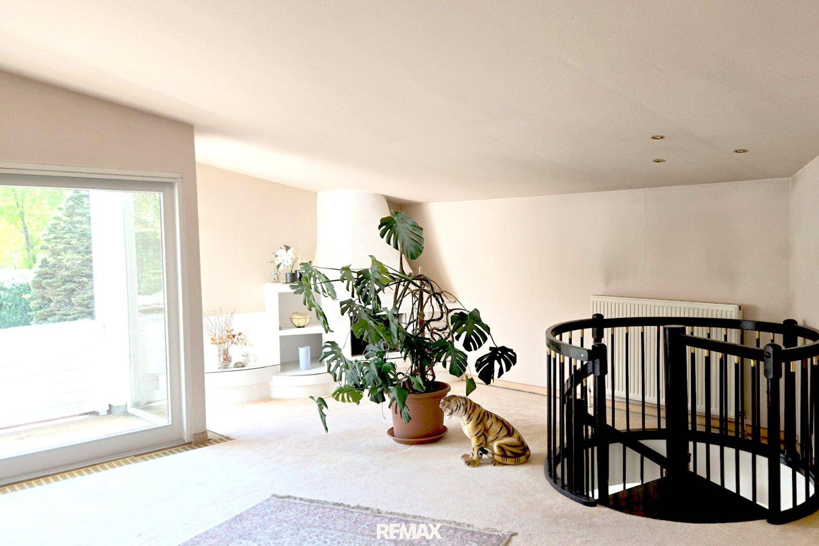 Geräumiges Wohnzimmer mit Kamin, großer Pflanze und einer eleganten Wendeltreppe zum Untergeschoss.