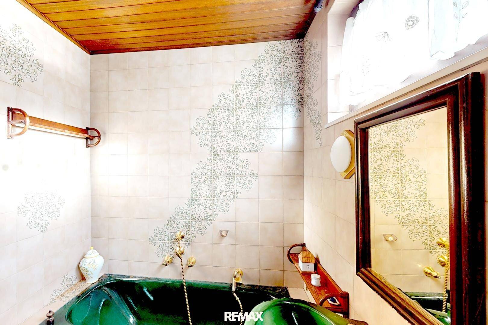 Badezimmer im Vintage-Stil mit grüner Badewanne, gemusterten Fliesen und Holzdecke.