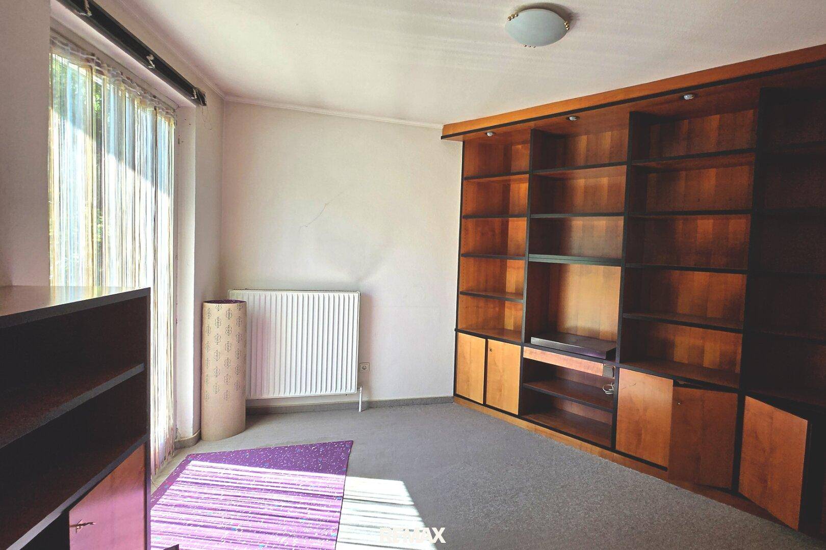 Arbeitszimmer mit großen, eingebauten Holzregalen, Teppichboden und viel natürlichem Licht.