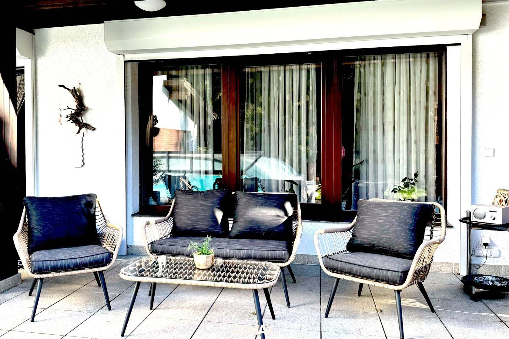 Gemütlicher Außenbereich auf einer gefliesten Terrasse mit modernen Gartenmöbeln und Rollläden.