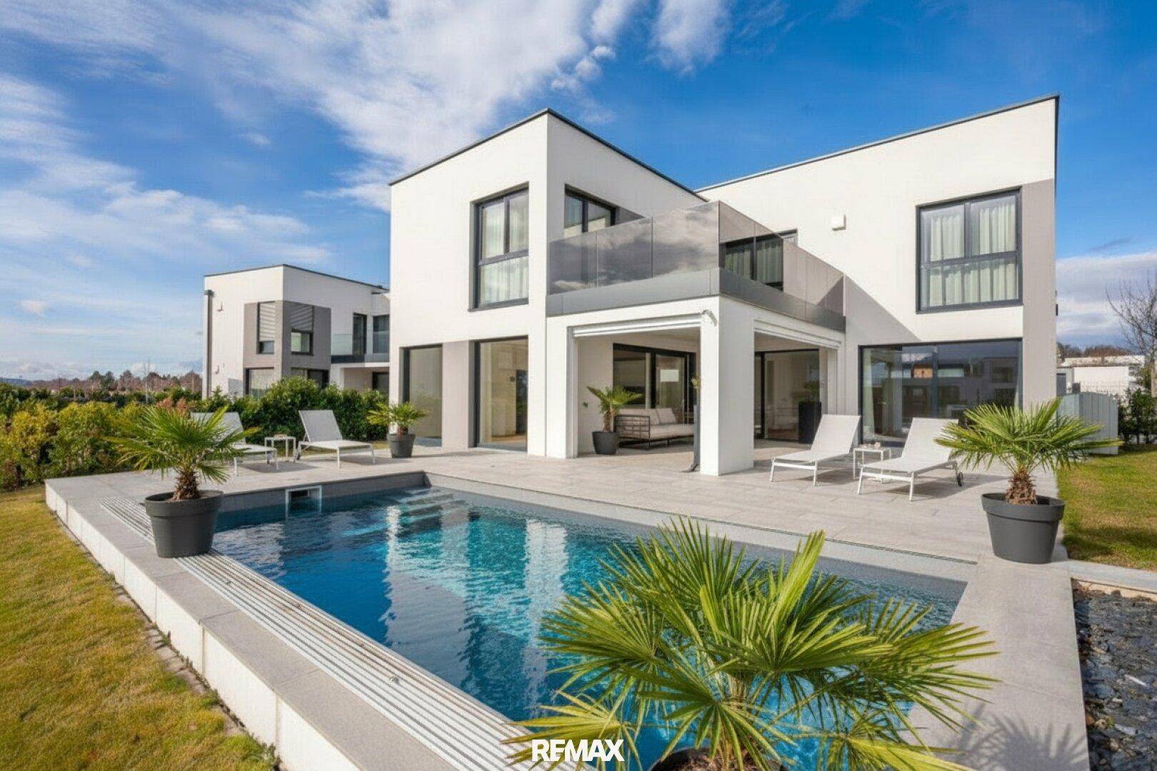 Moderne weiße Villa mit privatem Pool und gepflegtem Garten unter strahlend blauem Himmel.