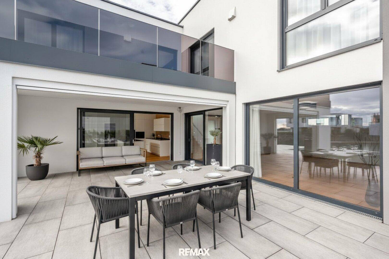 Großzügige Terrasse mit Esstisch und Zugang zu den hellen Innenräumen durch Glasschiebetüren.