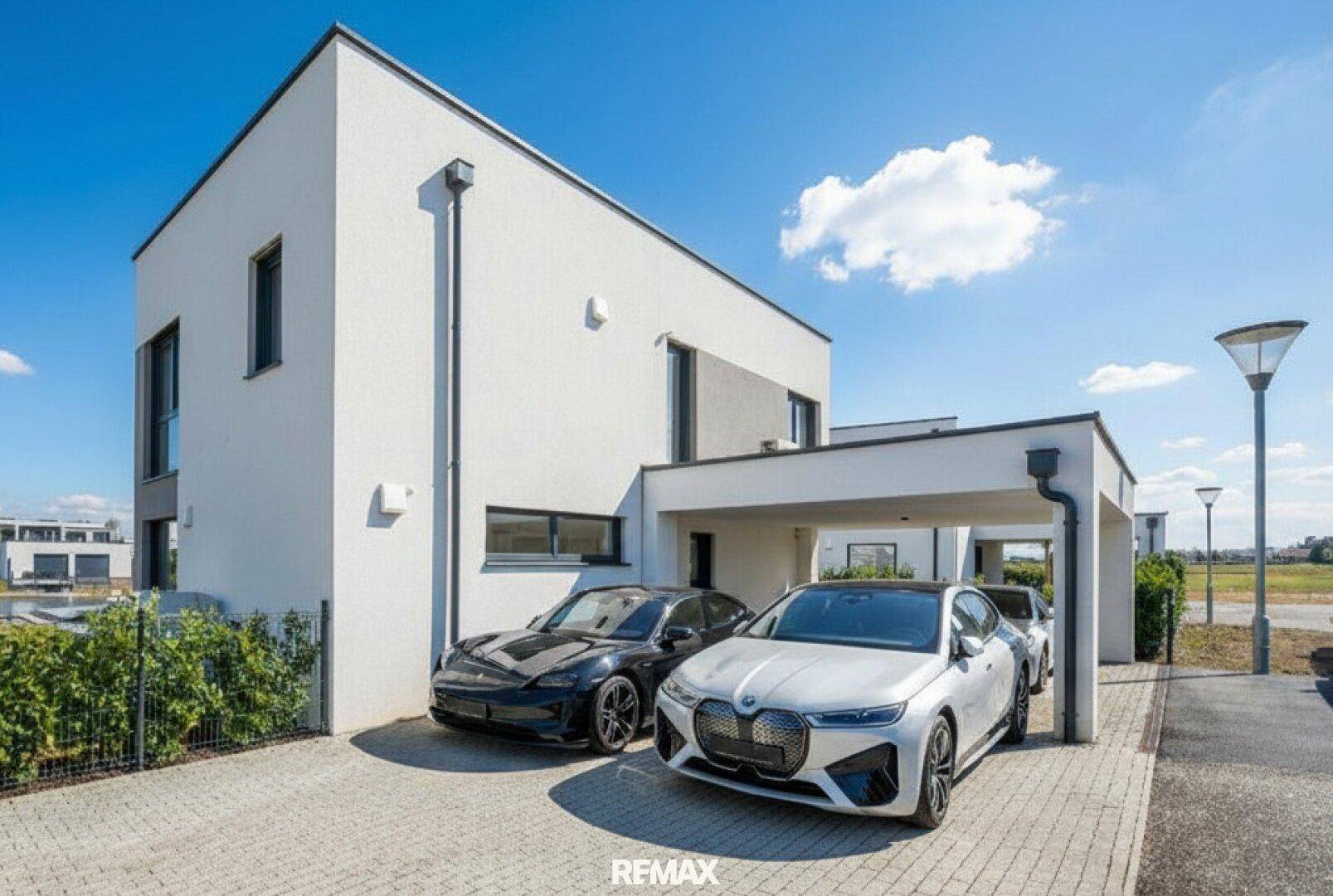 Moderne Hausfassade mit integriertem Carport und gepflasterter Auffahrt für mehrere Fahrzeuge.