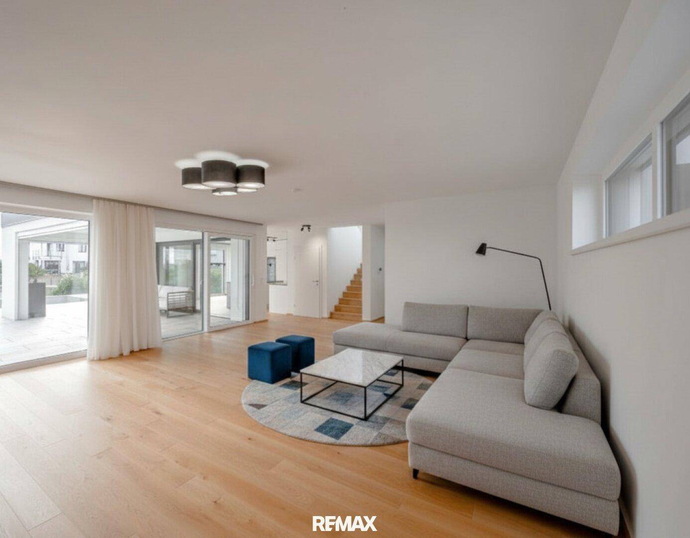 Geräumiges Wohnzimmer mit bequemer Couch, Holzboden und großen Schiebetüren zur Terrasse.