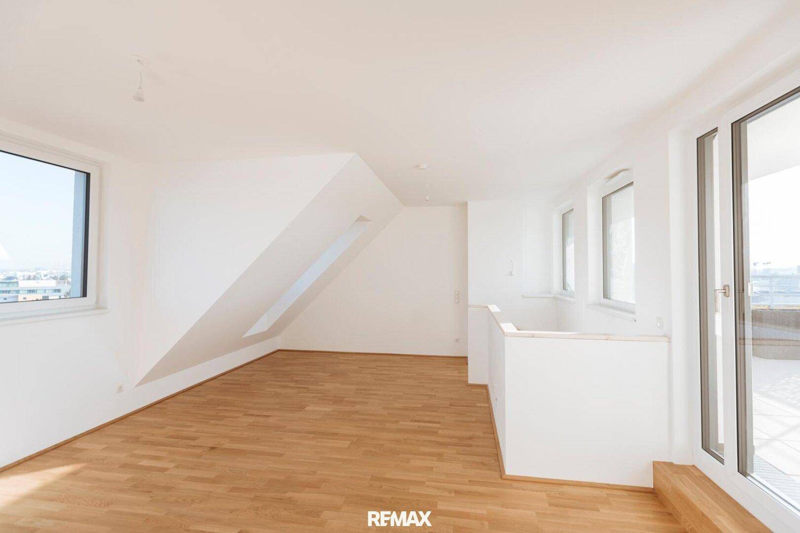 Geräumiger, heller Raum mit Holzboden, Dachschräge und Zugang zu einem Außenbereich.