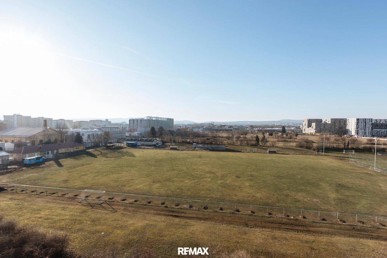 Panoramablick über eine weite Grünfläche mit städtischer Bebauung im Hintergrund.