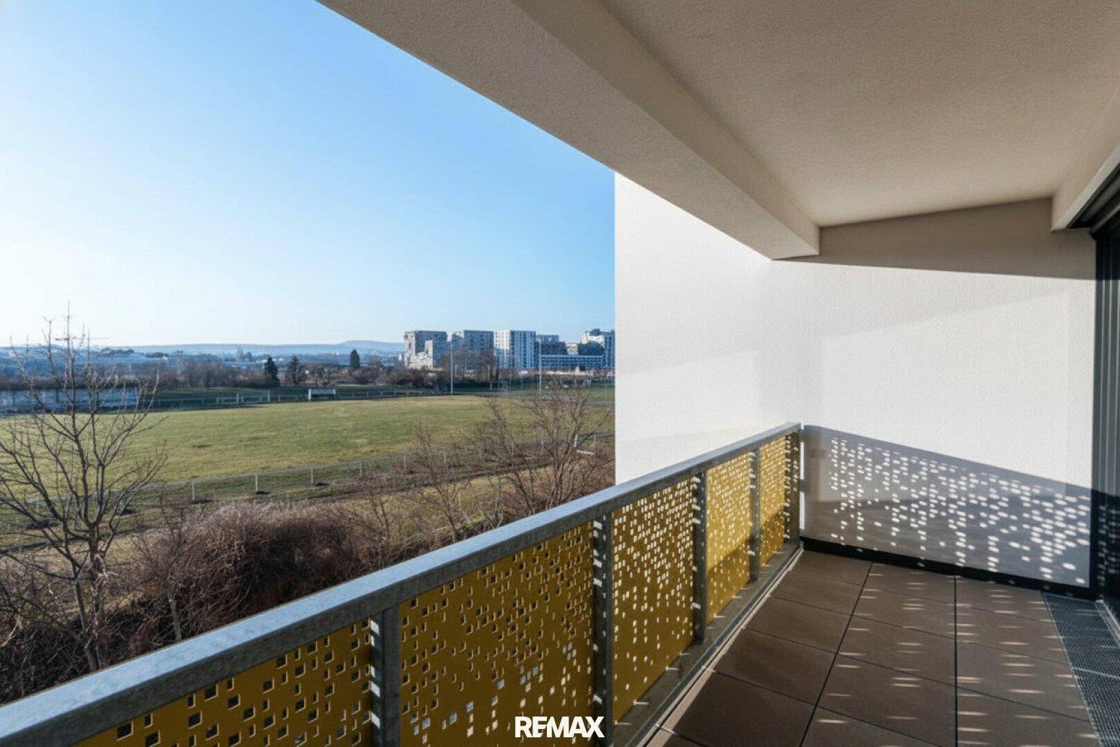 Heller Balkon mit dekorativem Geländer und weitem Blick über eine Grünfläche.