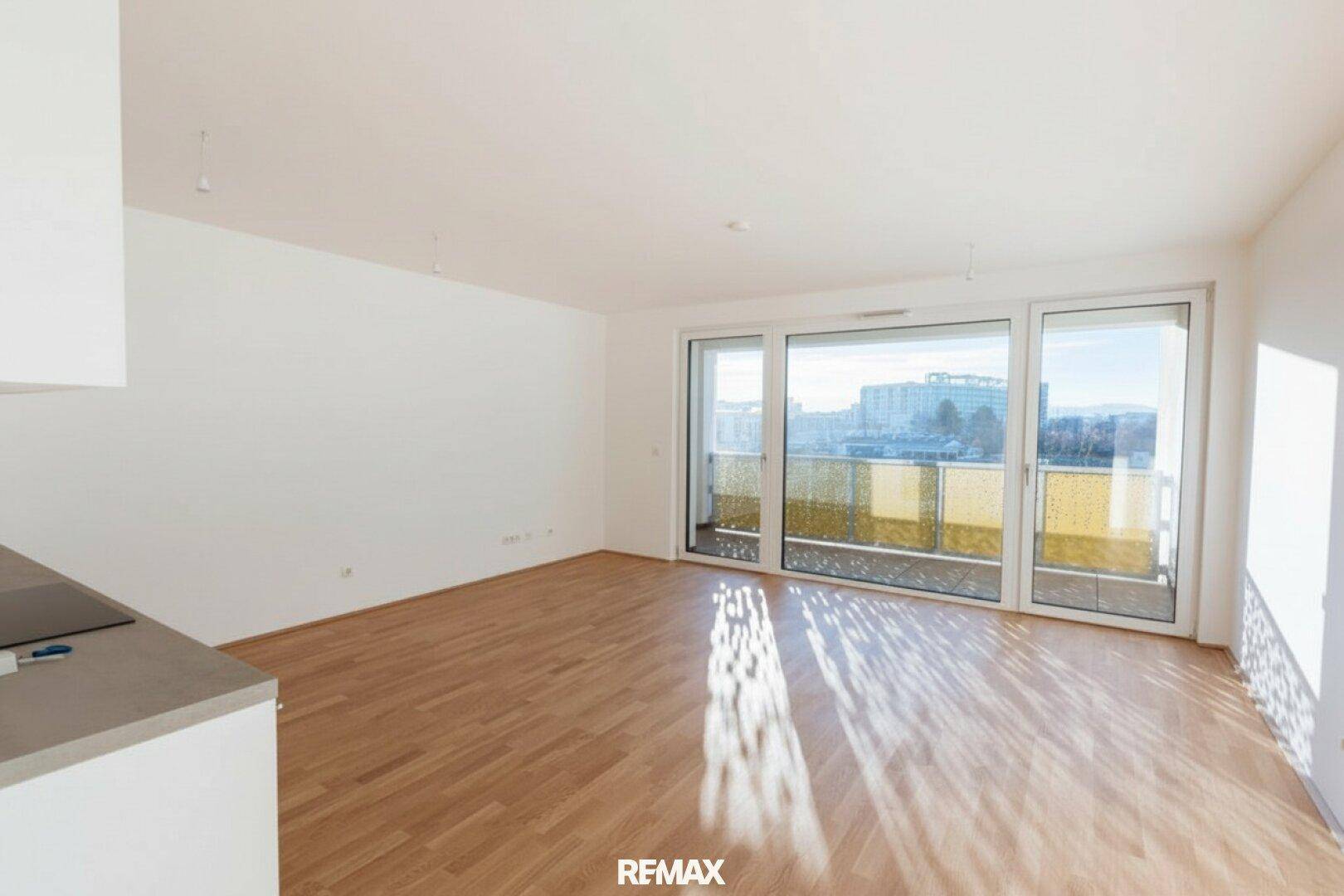 Heller, offener Wohnbereich mit Parkettboden und Zugang zu einem sonnigen Balkon.