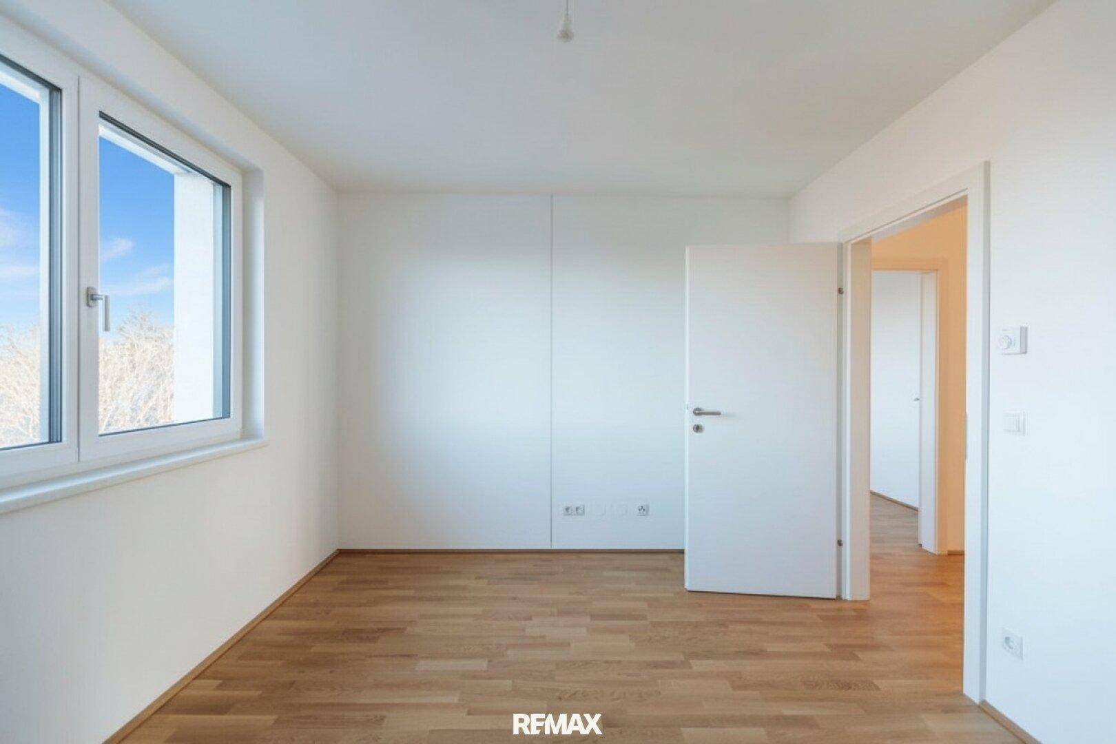 Geräumiges Schlafzimmer mit hellem Parkettboden und großen Fenstern.