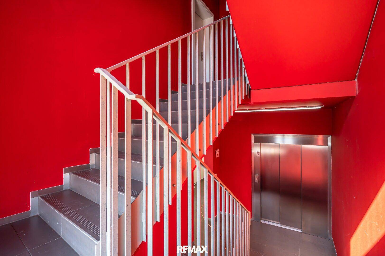 Treppenhaus mit leuchtend roten Wänden und einem modernen Aufzug.