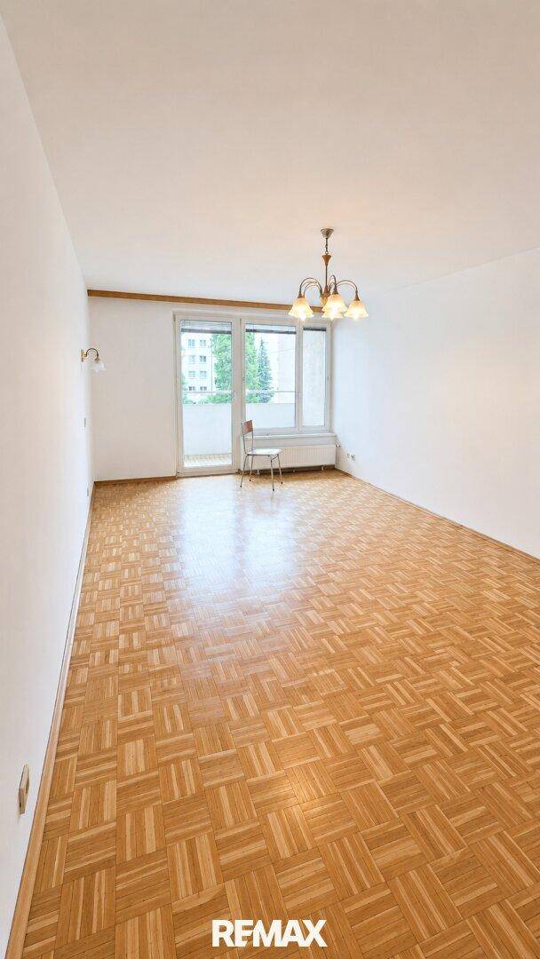 Geräumiges Wohnzimmer mit Parkettboden, Zugang zum Balkon und viel Tageslicht.