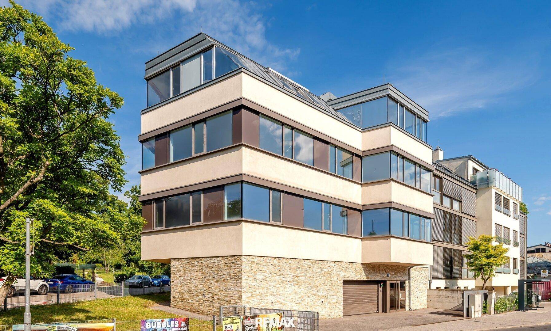 Moderne Architektur des Gebäudes mit großen Glasflächen und beiger Fassade unter blauem Himmel.