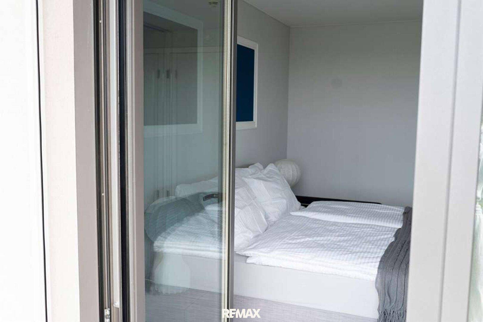 Schlafzimmer mit Doppelbett und weißer Bettwäsche, gesehen durch eine moderne Glastür.