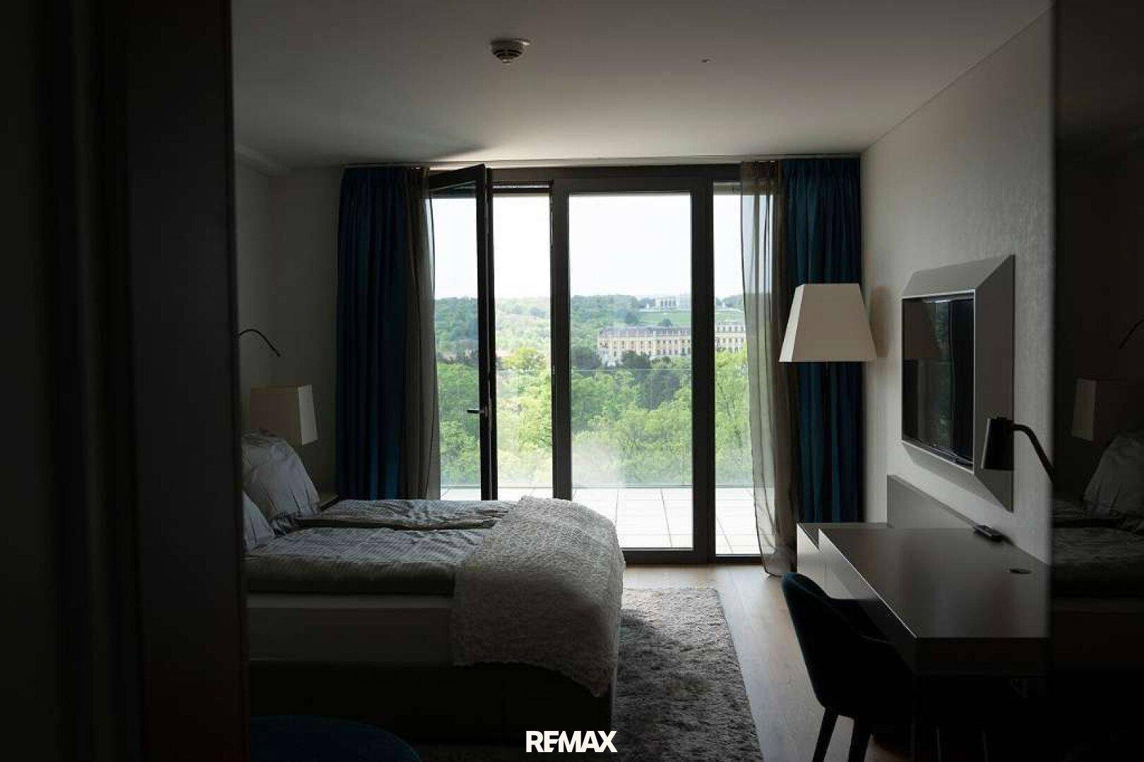 Schlafzimmer mit Doppelbett und großen Glasfronten, die einen weiten Blick ins Grüne bieten.