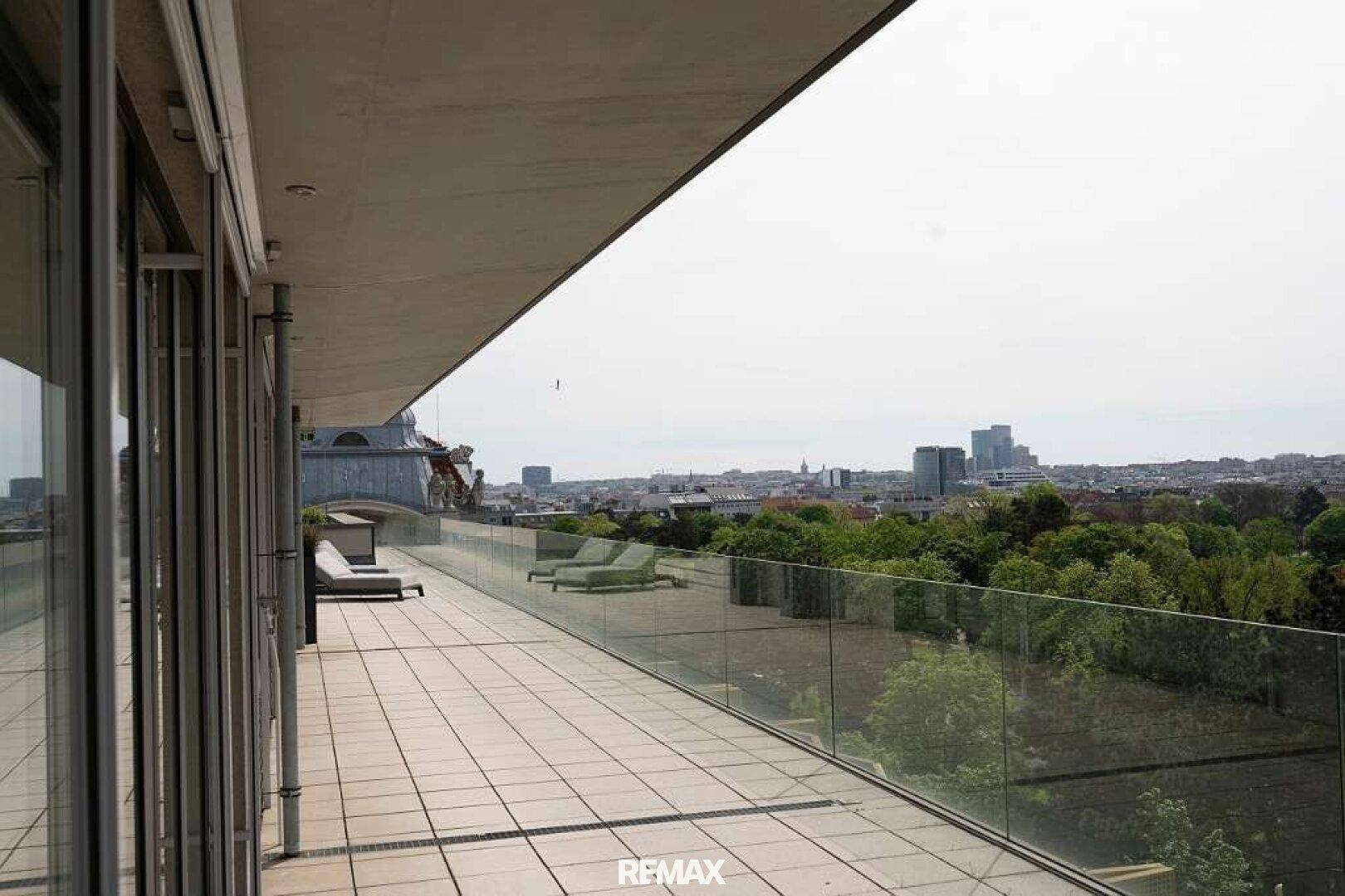 Lange Außenterrasse mit Fliesenboden, Glasgeländer und weitem Blick auf die Stadtlandschaft.