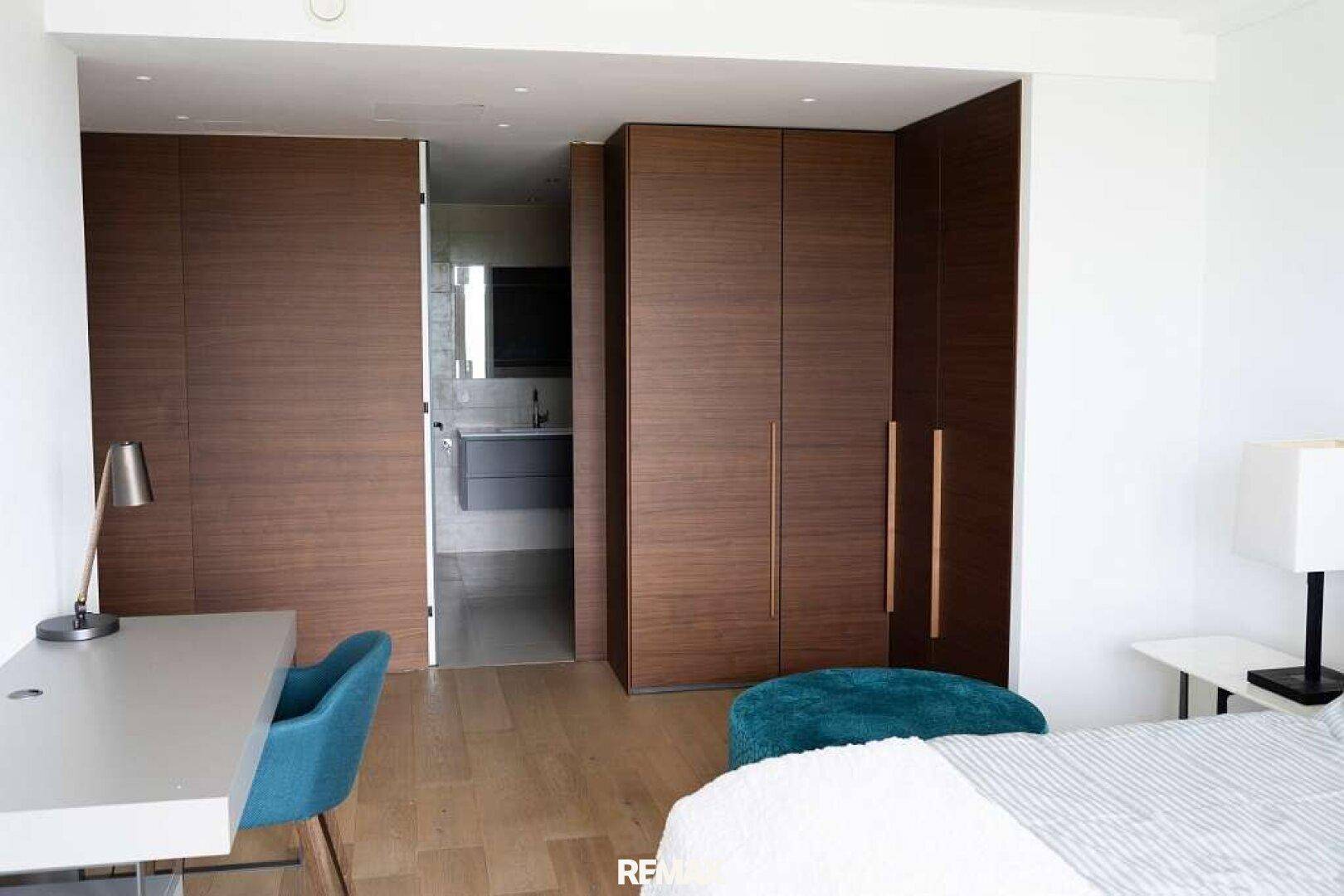 Schlafzimmer mit eingebauten Holzschränken und Blick in ein angrenzendes Badezimmer.