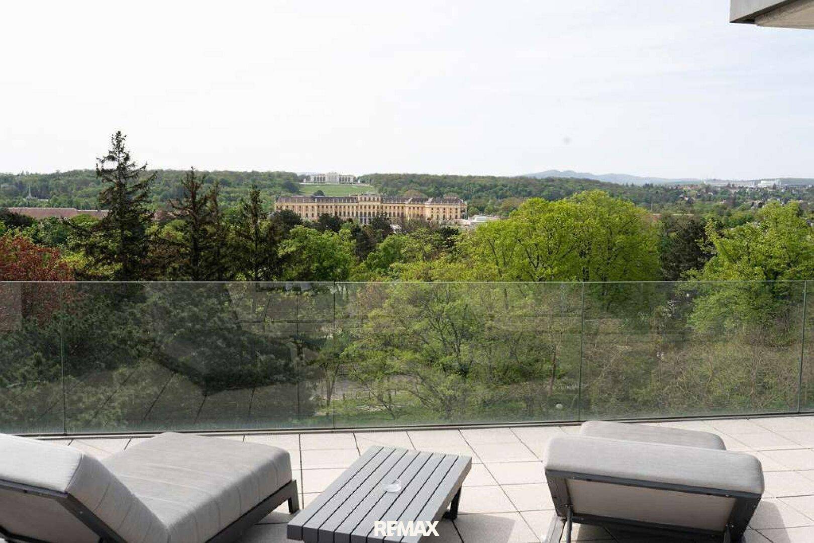 Geräumige Terrasse mit Liegestühlen und einem Tisch, bietet einen weiten Blick auf das Schloss Schönbrunn und viel Grün.