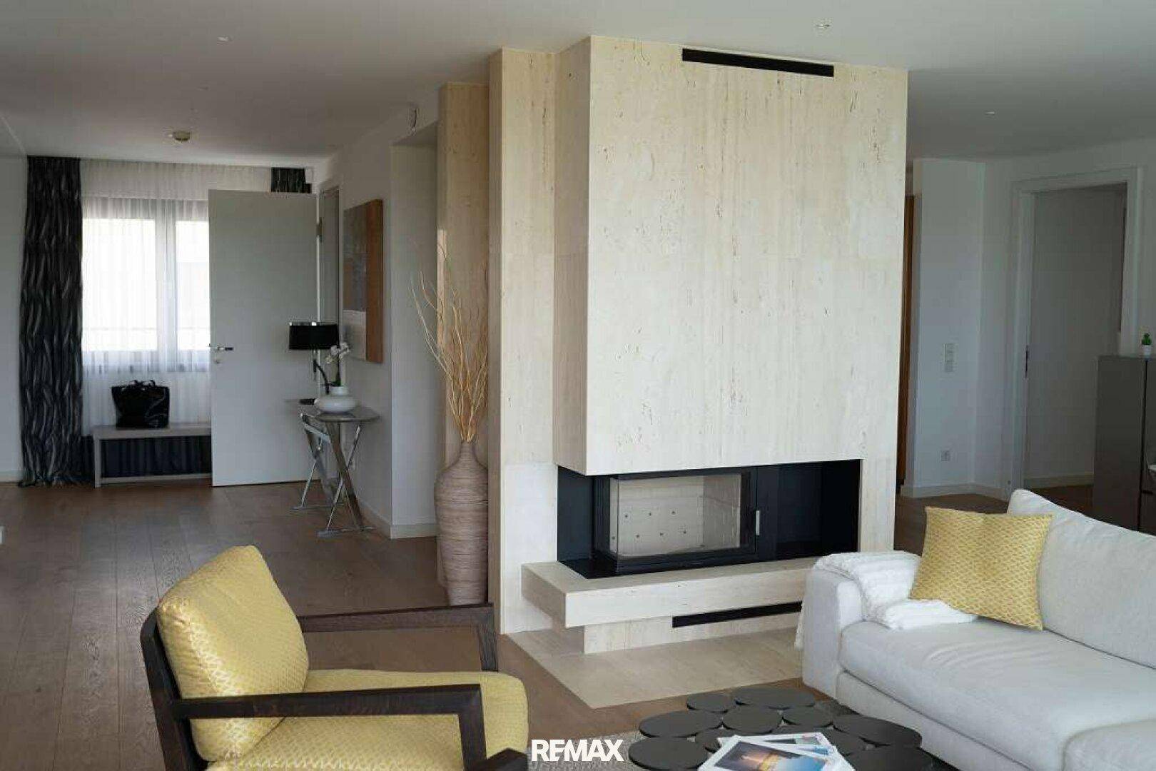 Gemütliches Wohnzimmer mit modernem Kamin, weißem Sofa und gelbem Sessel, auf hellem Parkettboden.