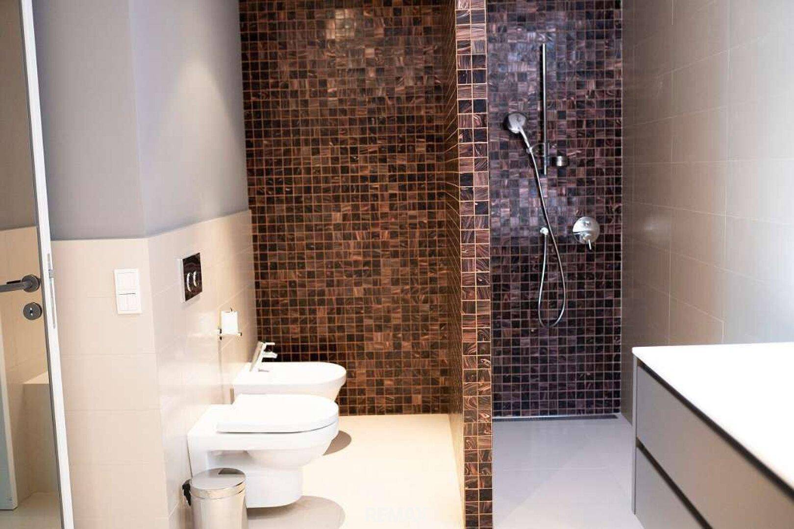 Modernes Badezimmer mit Toilette, Bidet und einer begehbaren Dusche mit Mosaikfliesen.
